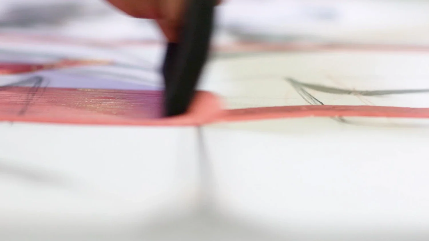 Close-up of a black pen writing or drawing on a sheet of paper with printed text or graphics.