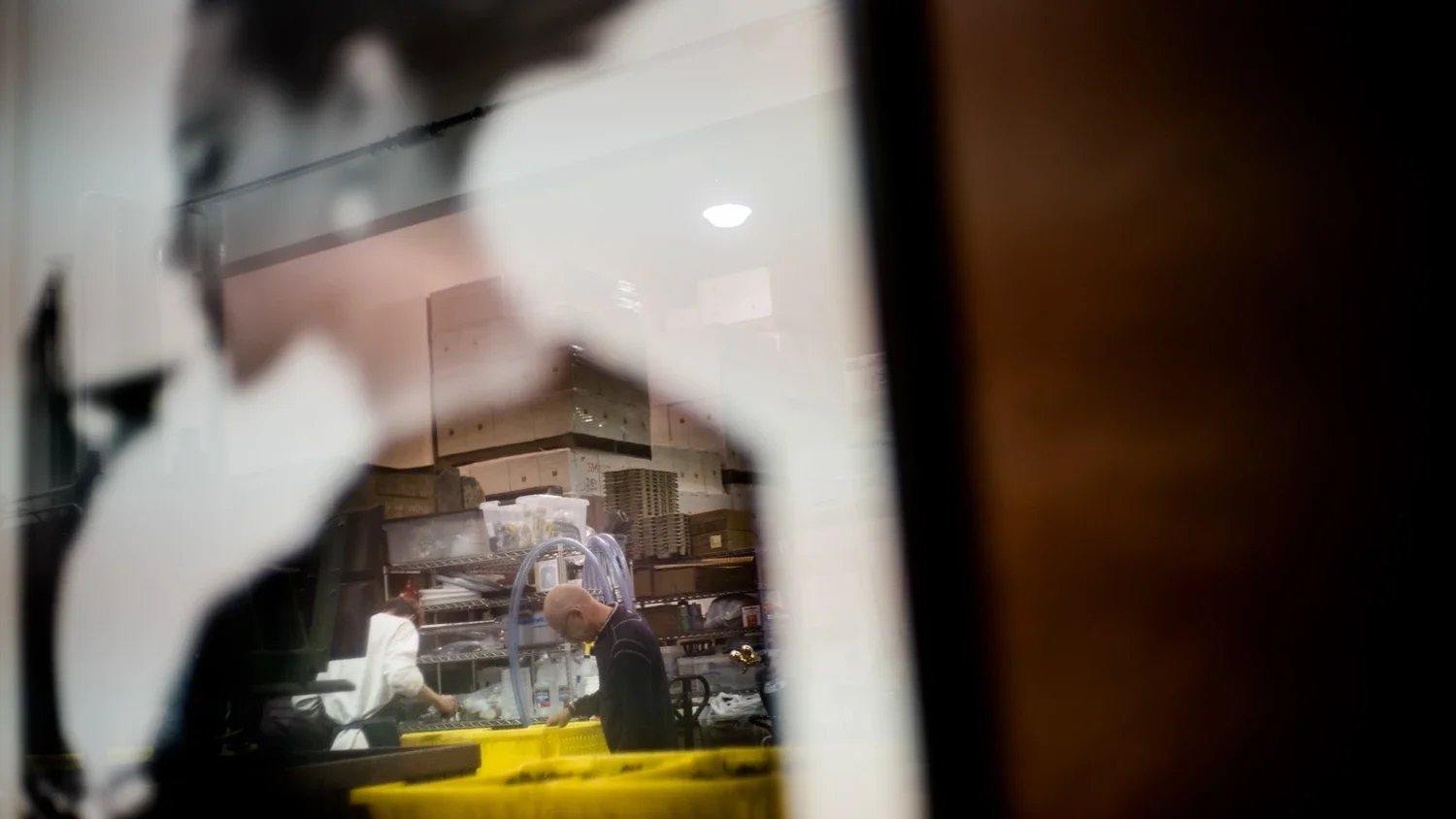 Bill Wenzlau inspecting the grapes inside the yellow bins in his winery, seen through an iconic image of the woman drinking a glass of wine