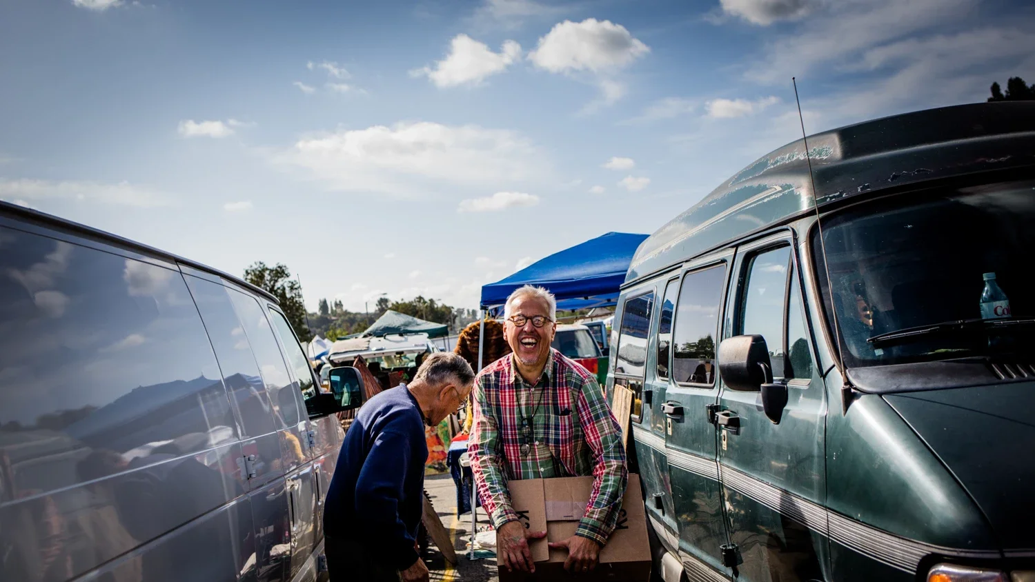Jim Heimann between old vans laughing as he received a box of paper ephemera from someone at the swap meet