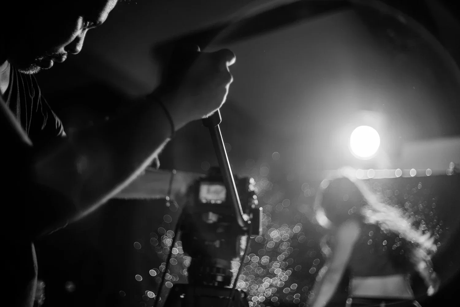 A person operating a camera at night with bright lights and bokeh effects in the background.