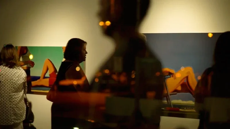 People viewing modern artwork at an art gallery, with reflections of city lights in the glass.