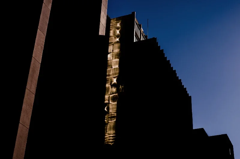 Tall modern building with reflective windows against a dark blue sky, illuminated by sunlight.