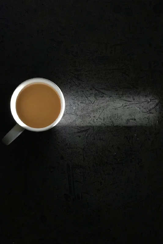 A white mug filled with coffee on a dark textured surface.