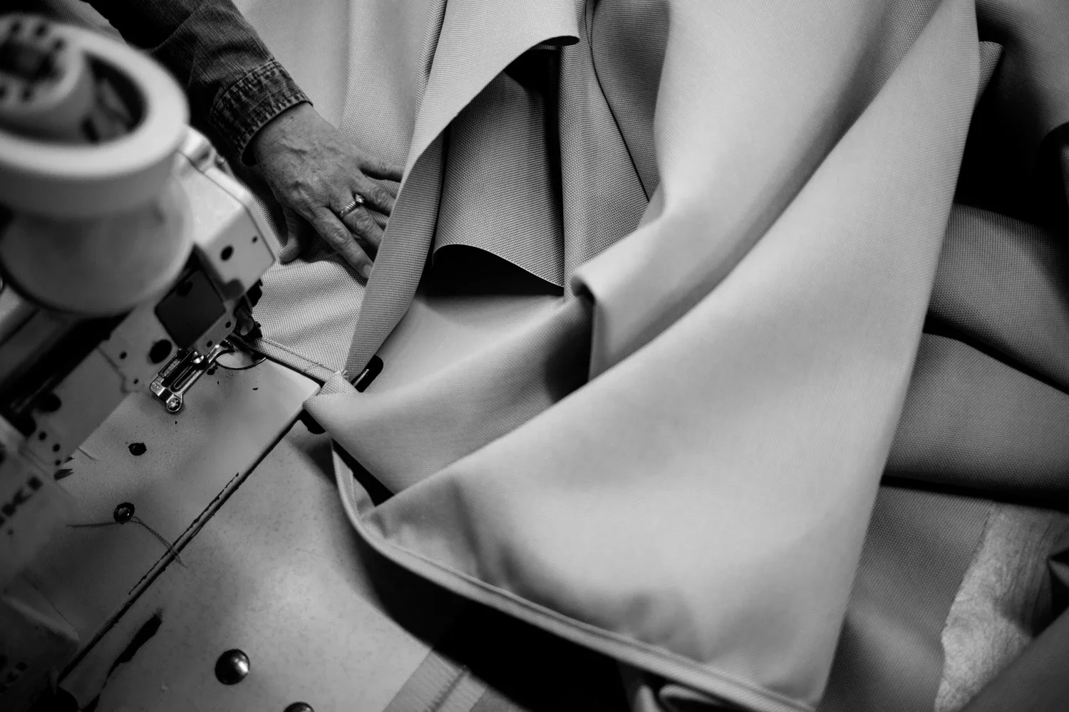 A woman's hand is seen advancing the material of a outdoor furniture umbrella on a knitting machine