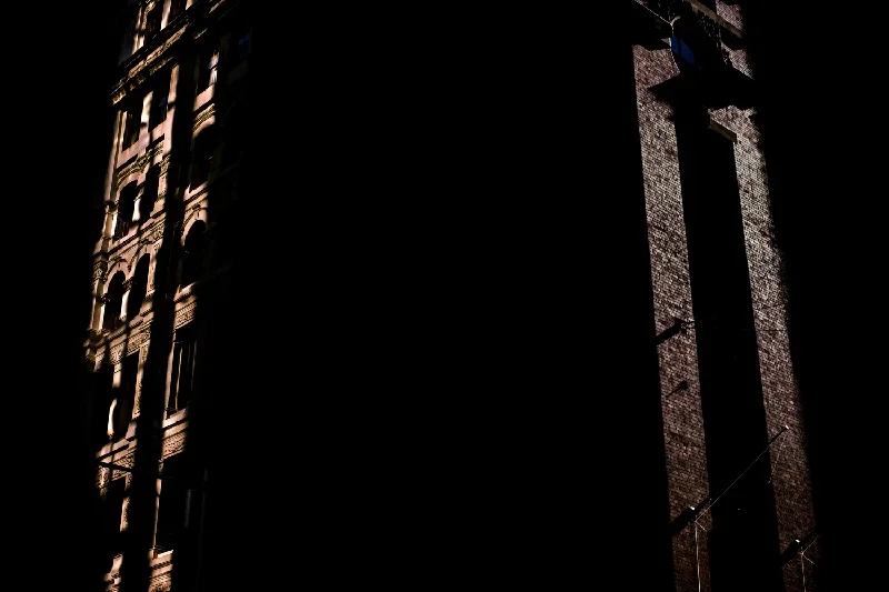 Partial view of two tall buildings with intricate windows and brick exteriors, mostly shrouded in darkness.
