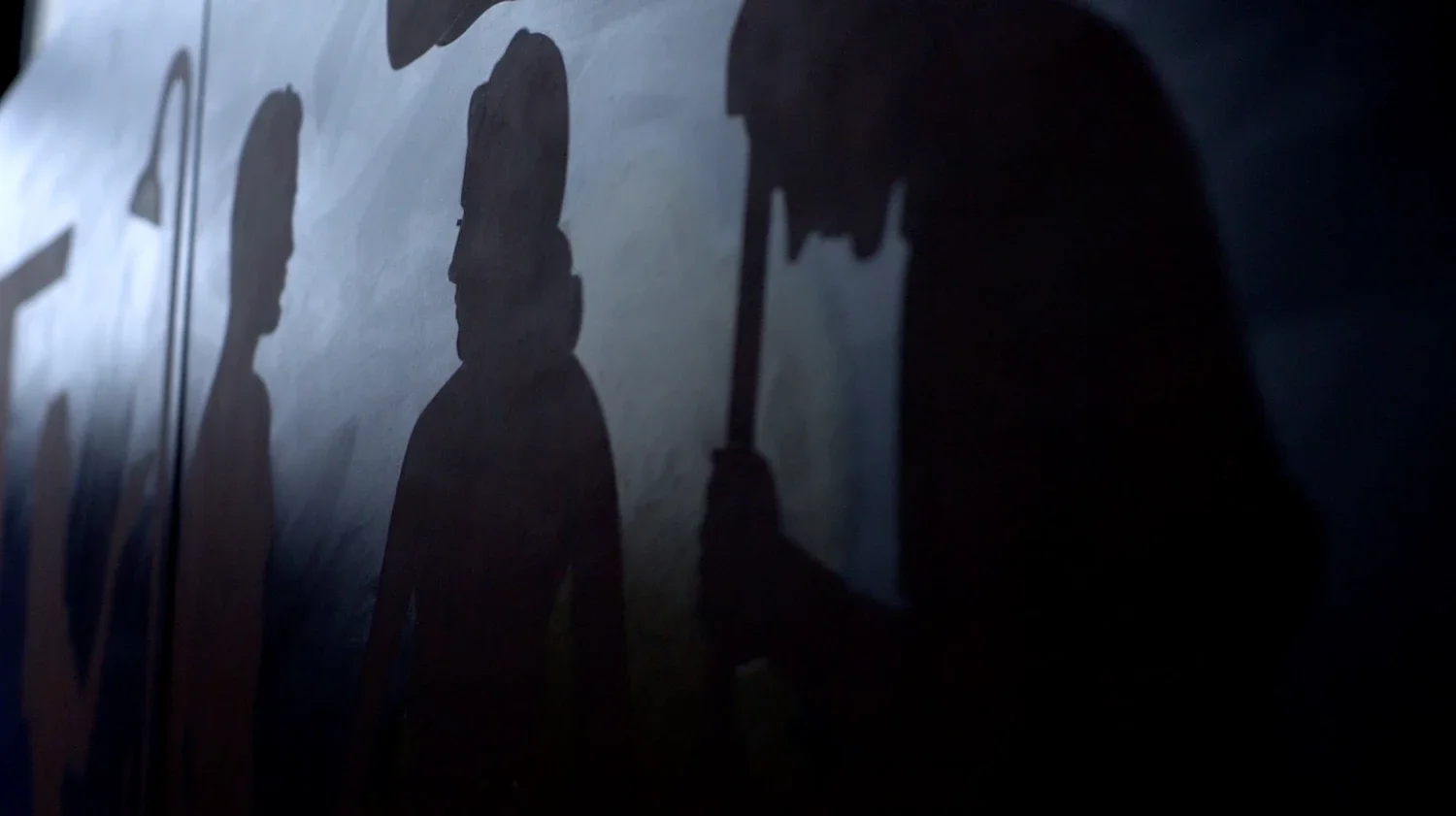 Silhouette of a person holding an umbrella on a dark wall.