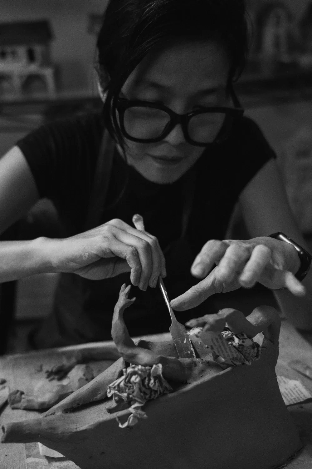 A woman with dark hair and glasses is eating from a bowl using a fork. The scene is in black and white.