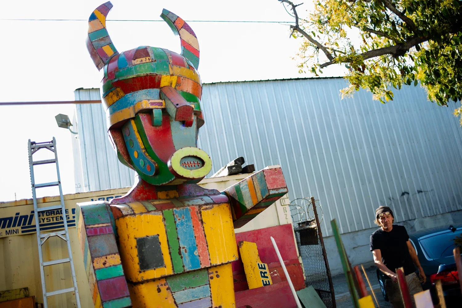 giant metal sculpture resembling a tribal character in multi color metal pieces