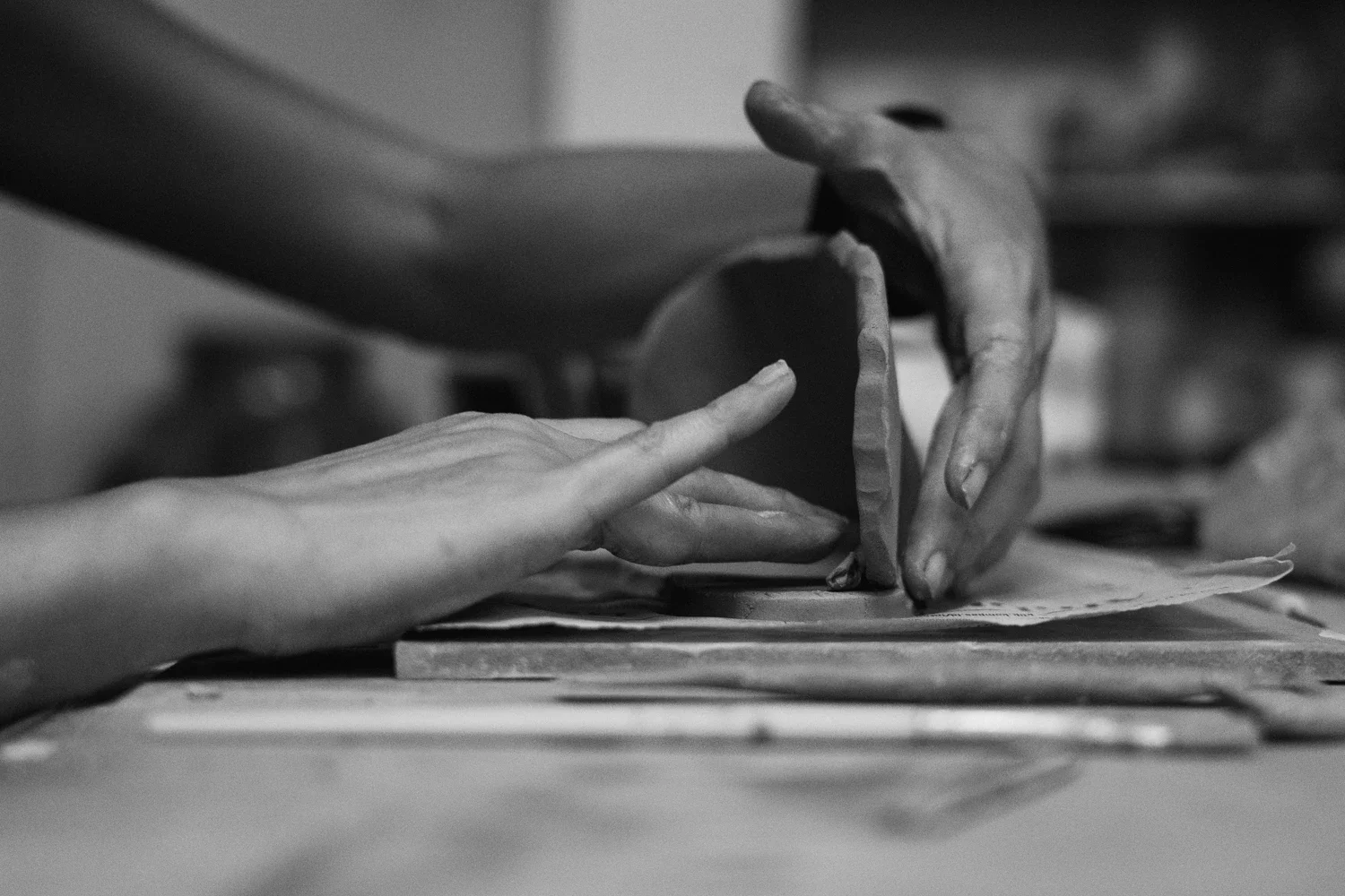 Close-up of two hands working on a pottery project, one hand shaping clay and the other hand supporting, black and white photo.