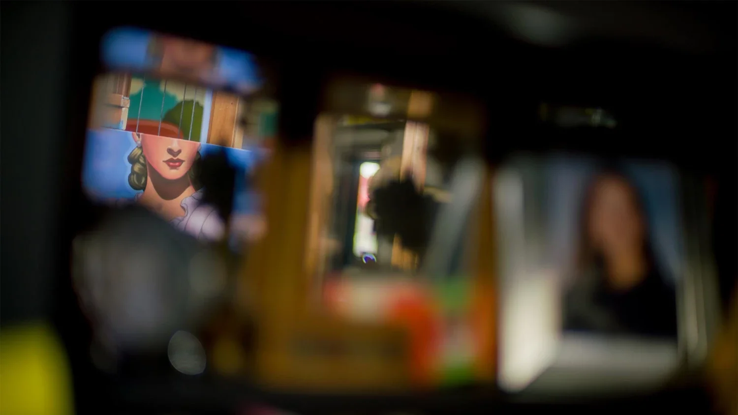 Blurred reflections of artworks, including a woman with blonde hair, in a mirror or glass surface.
