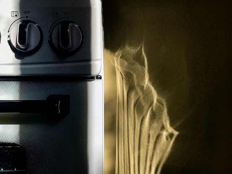 Close-up of a metallic stovetop with two black control knobs, and a glowing X-ray of a skeleton on a dark background.