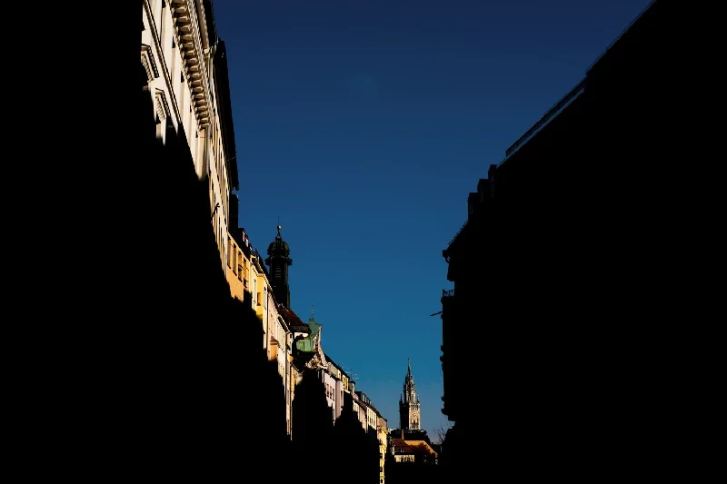 City street with historic buildings and towers silhouetted against a clear blue sky.