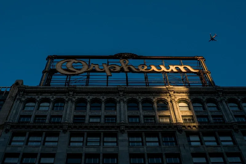 View of a building with a large illuminated sign on top that reads 'Cuphowm', with a blue evening sky in the background and a small aircraft flying overhead.