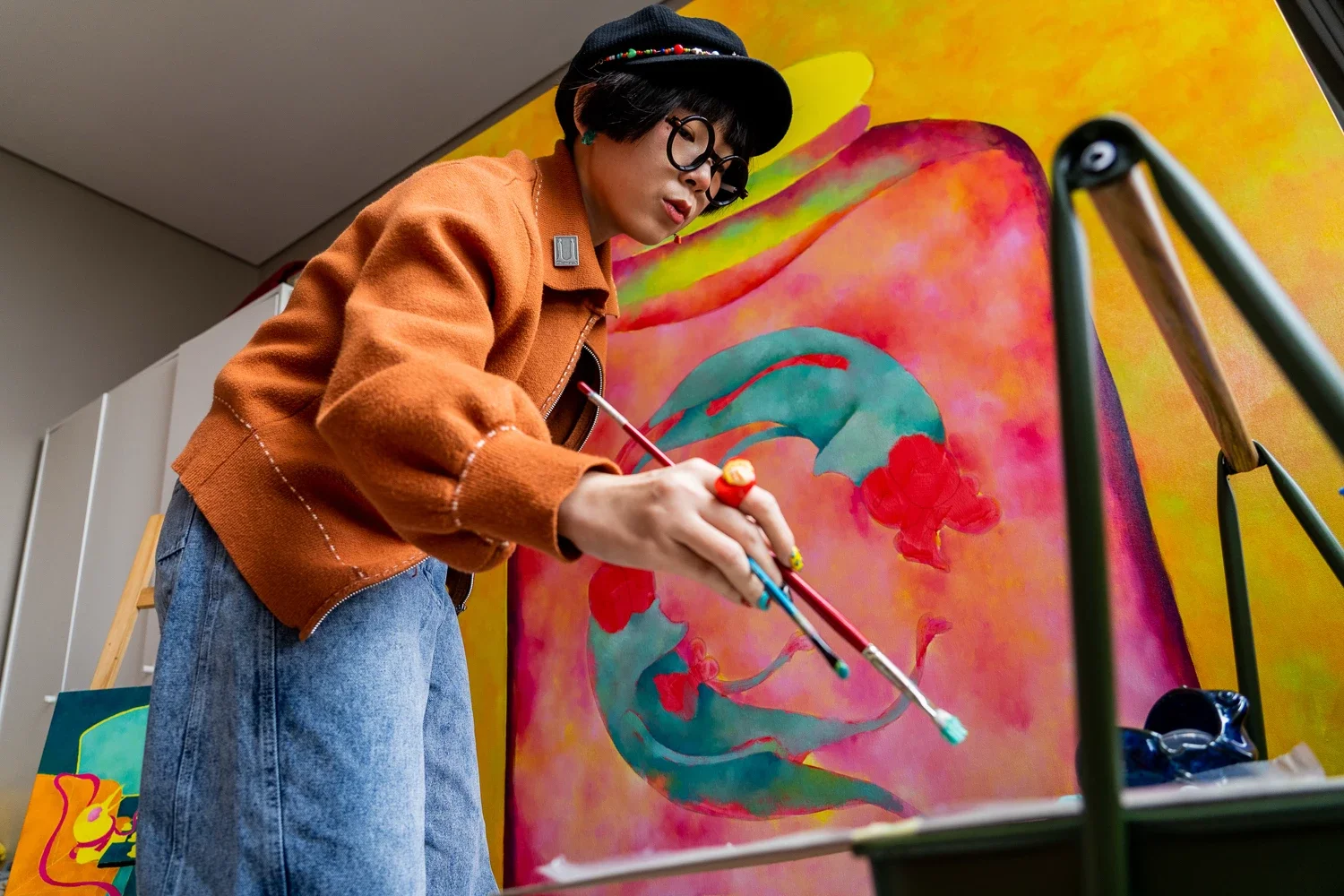 An artist painting a colorful abstract artwork with red, blue, and pink hues on a large canvas.
