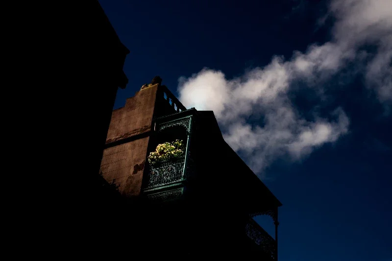 An upward view of a building with a balcony and potted plants, against a dark sky with clouds.