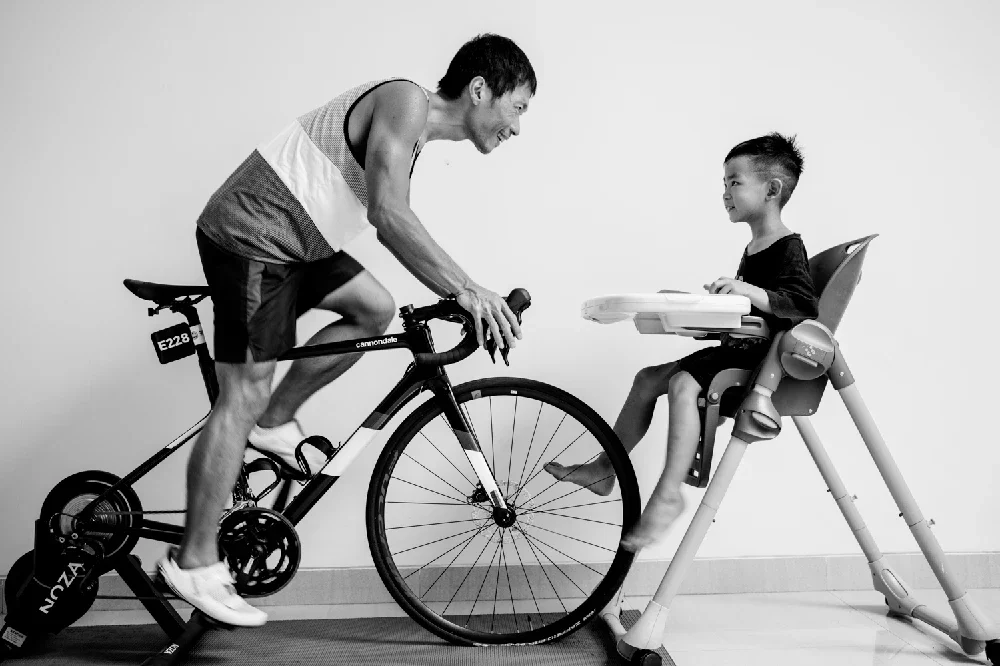 A man on a bicycle engaging with a young girl seated in a high chair.