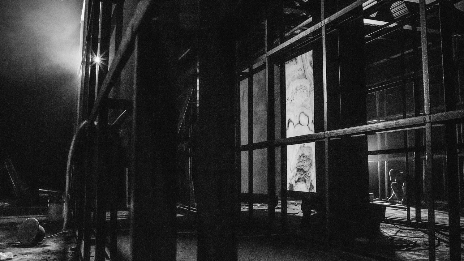 a piece of marble is installed in a construction area while back lit. behind it there is a person working on the floor taking measurements in the construction site