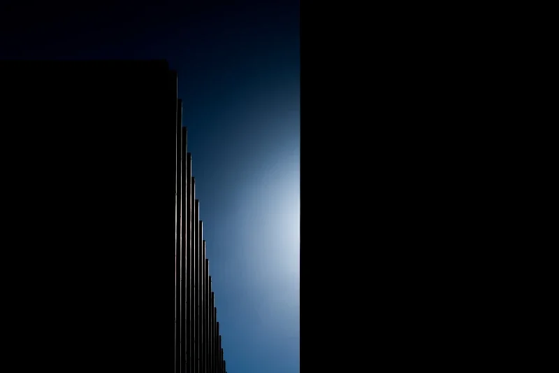 A silhouette of a tall building against a clear blue sky with the sun shining behind it.