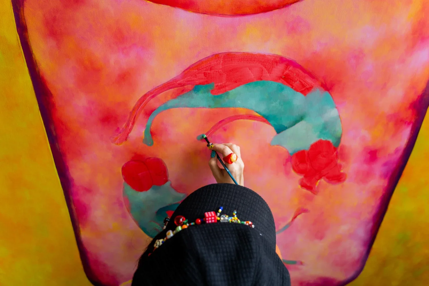 Artist painting a colorful abstract piece on a large canvas with pink, red, and green hues.