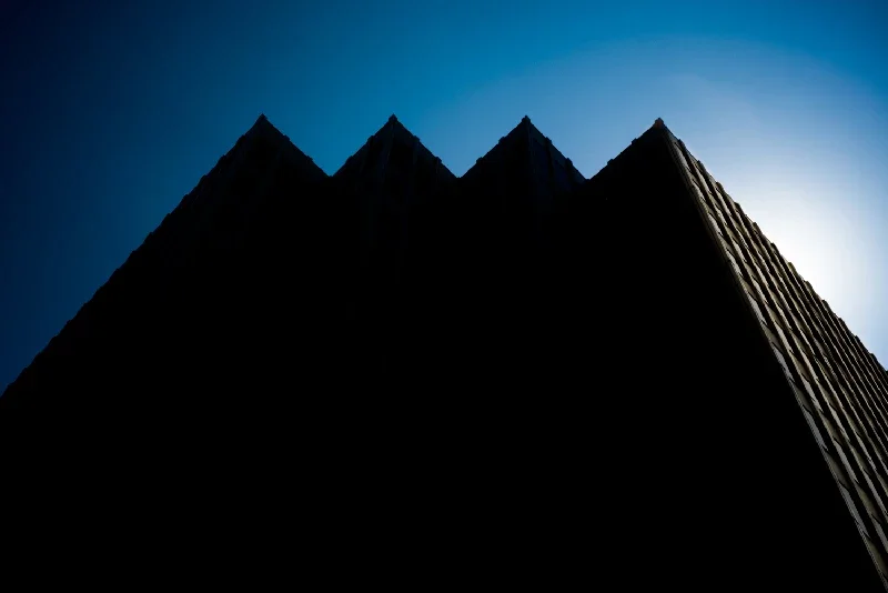 A tall building silhouette against a bright blue sky, viewed from below.