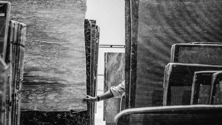 A hand guides a slab of finished marbe through other slabs of marble of different kinds