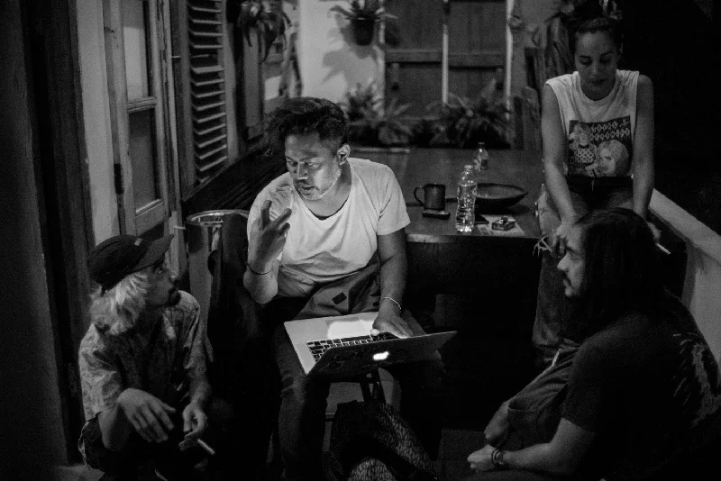 Three people gathering around Anton Ismael with a laptop, engaging in conversation in a cozy indoor setting.
