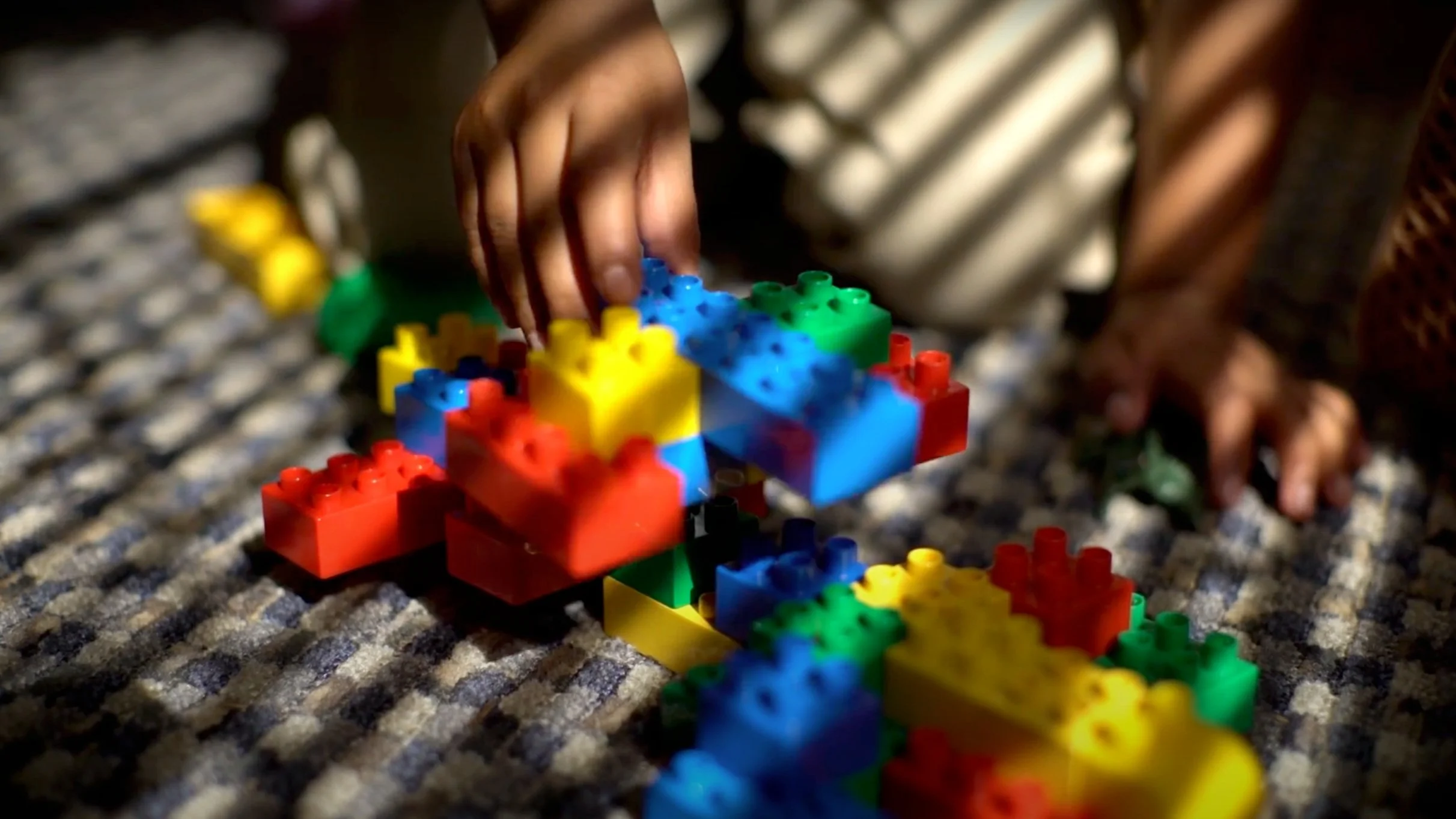 A child's hand building a colorful lego on a carpet streaks of light all over