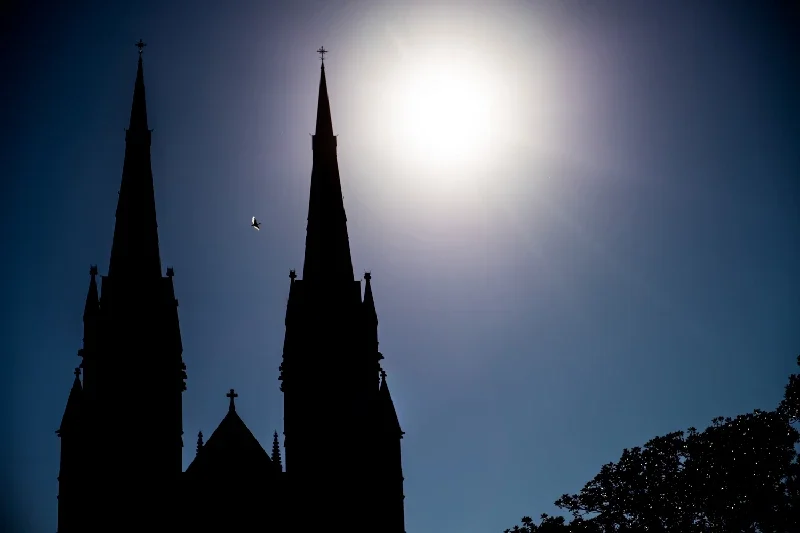 Silhouette of a church with two tall steeples against the bright sun and a clear sky.