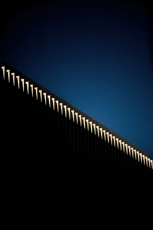 Close-up of a modern architectural structure with a row of illuminated white spikes against a dark and blue twilight sky.