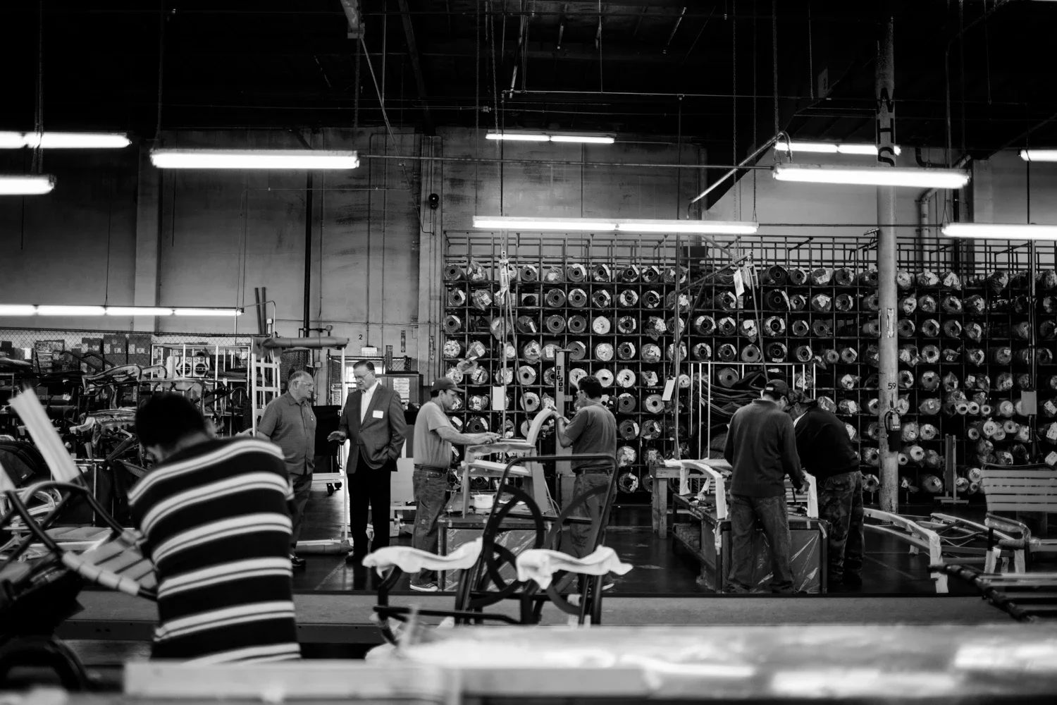 two people talking in the midst of people working on a furniture assembly area in a production floor.