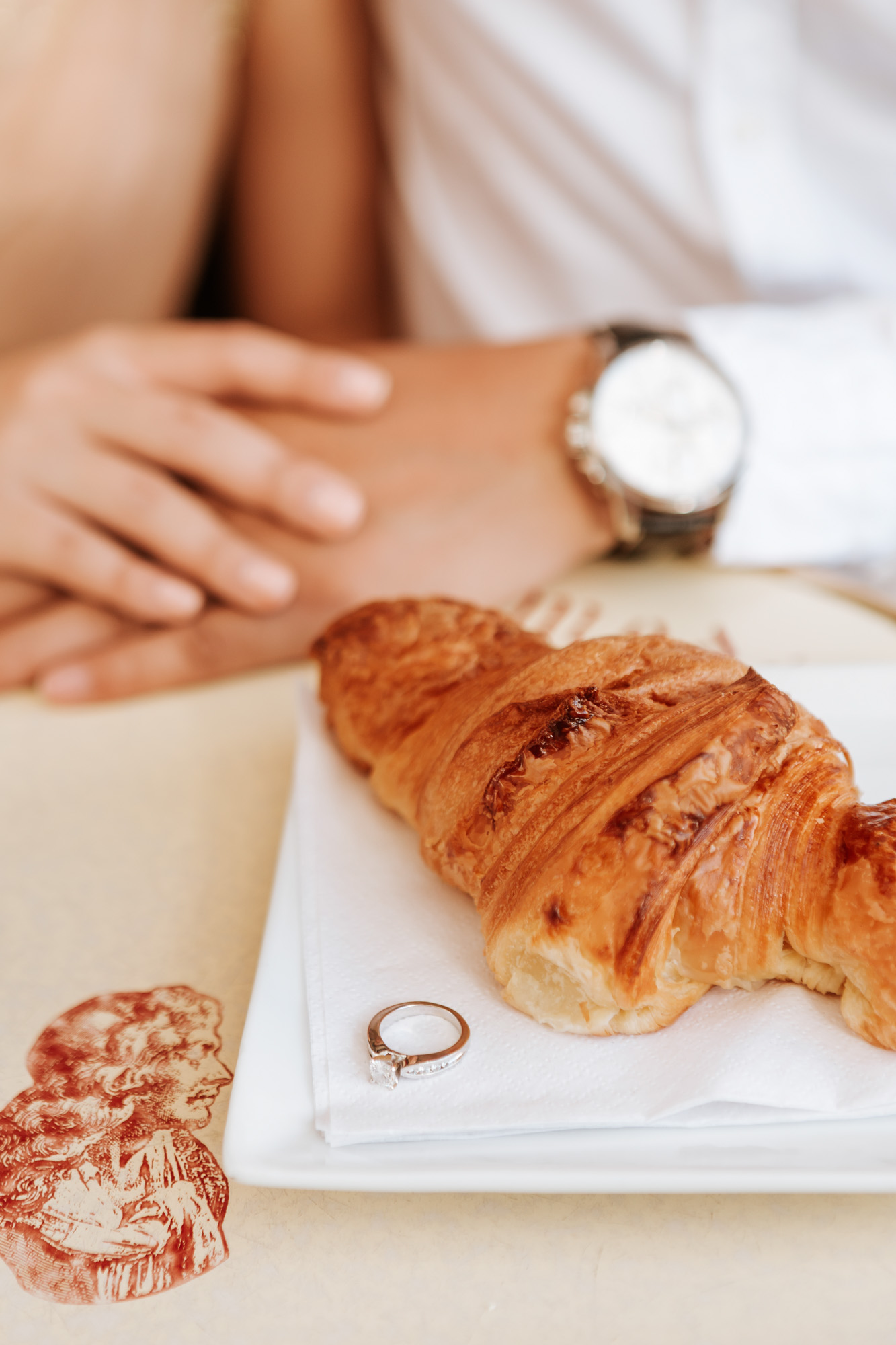 Pre-wedding diamond engagement ring next to coffee and croissant at cafe captured by Paris Photographer Federico Guendel