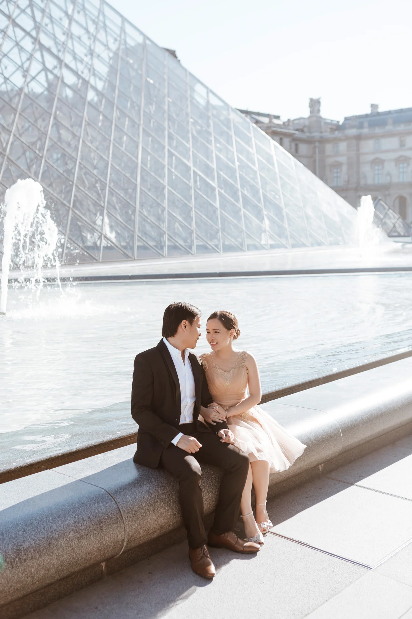 Pre-wedding couple portrait sitting by the Pyramid at the Louvre Museum captured by Paris Photographer Federico Guendel