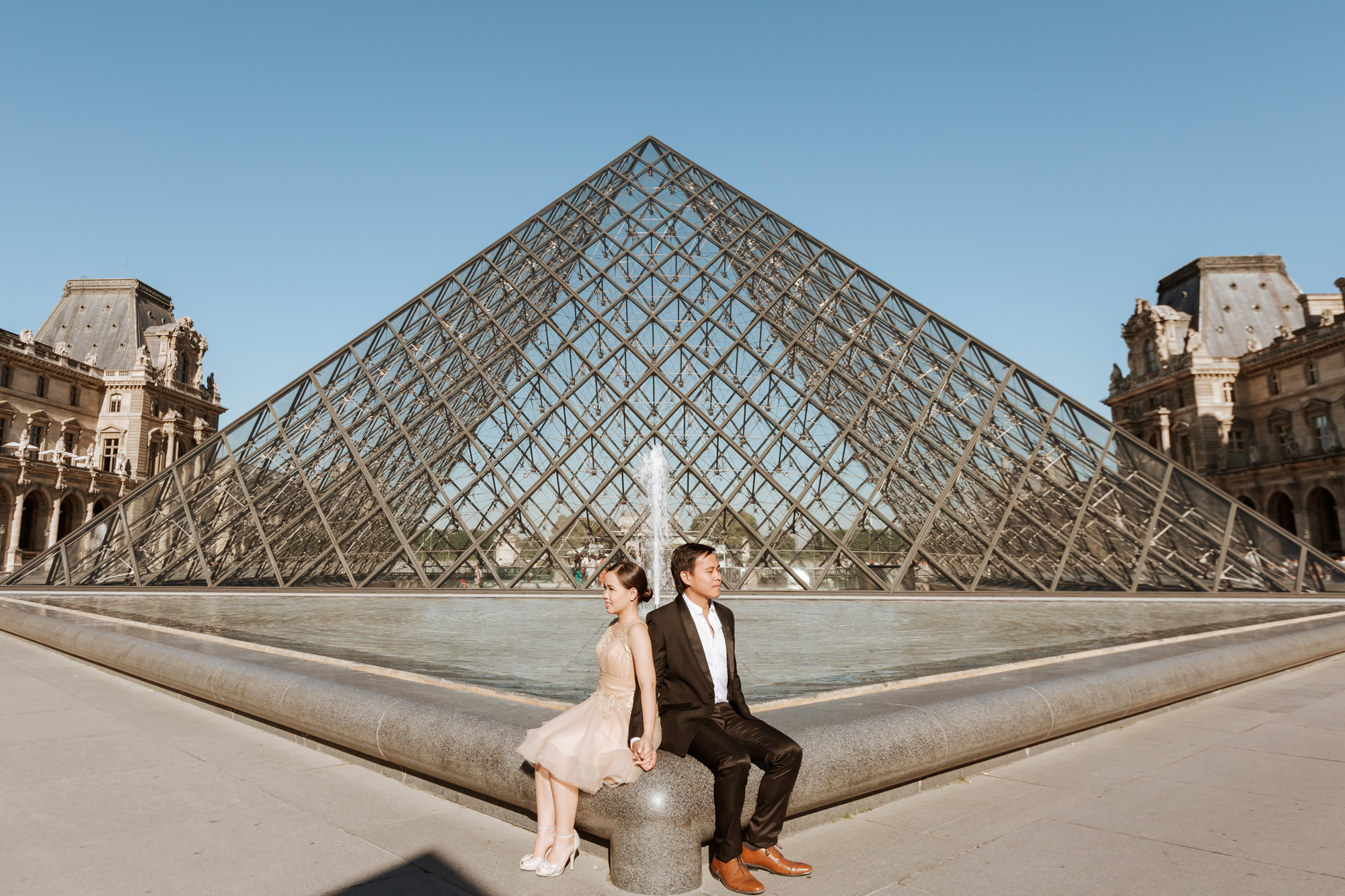 Pre-wedding couple portrait sitting by the Louvre Pyramid captured by Paris Photographer Federico Guendel