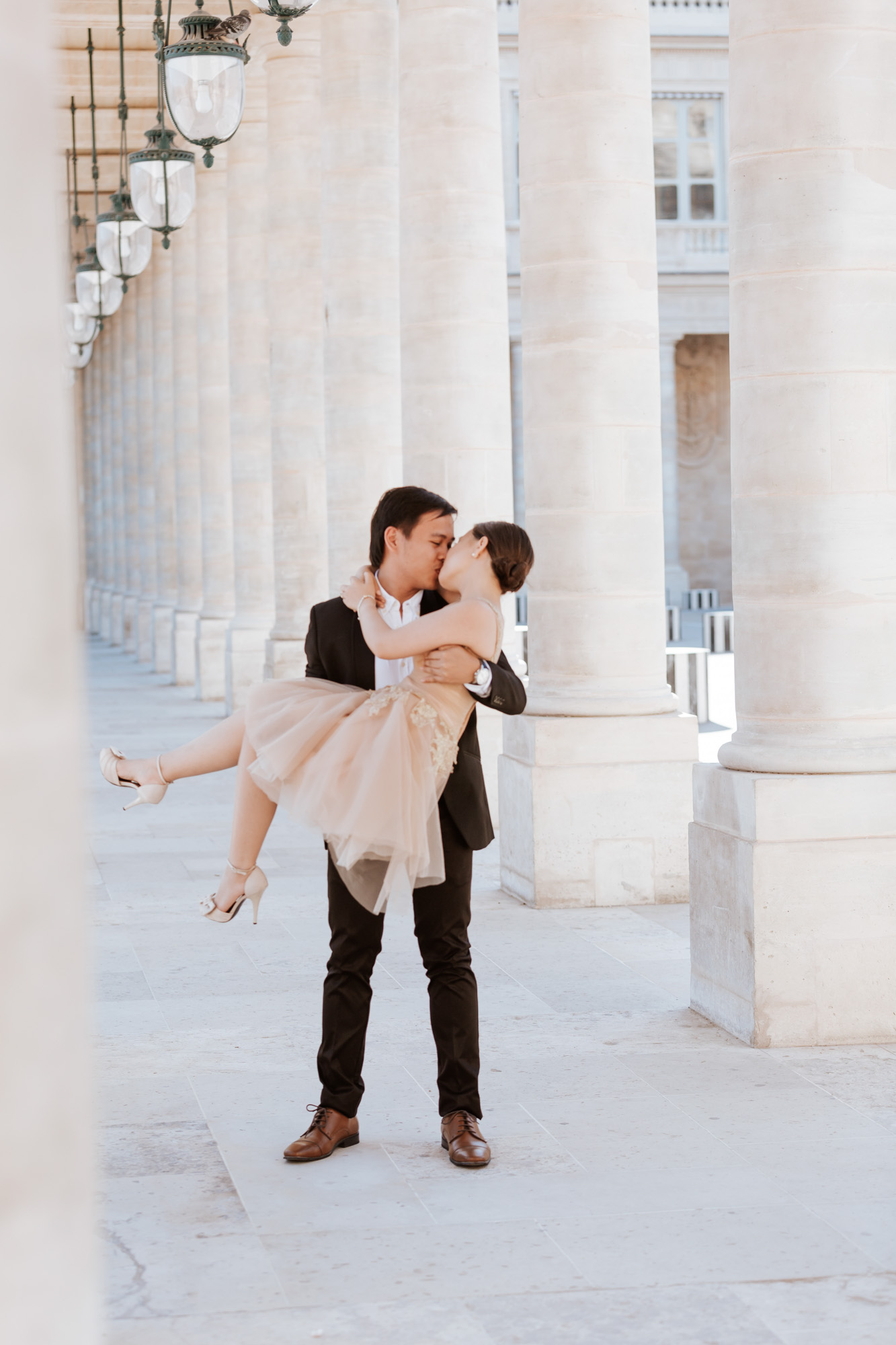 Groom holding bride in his hands by the columns at Palais Royal pre-wedding portrait captured by Paris Photographer Federico Guendel