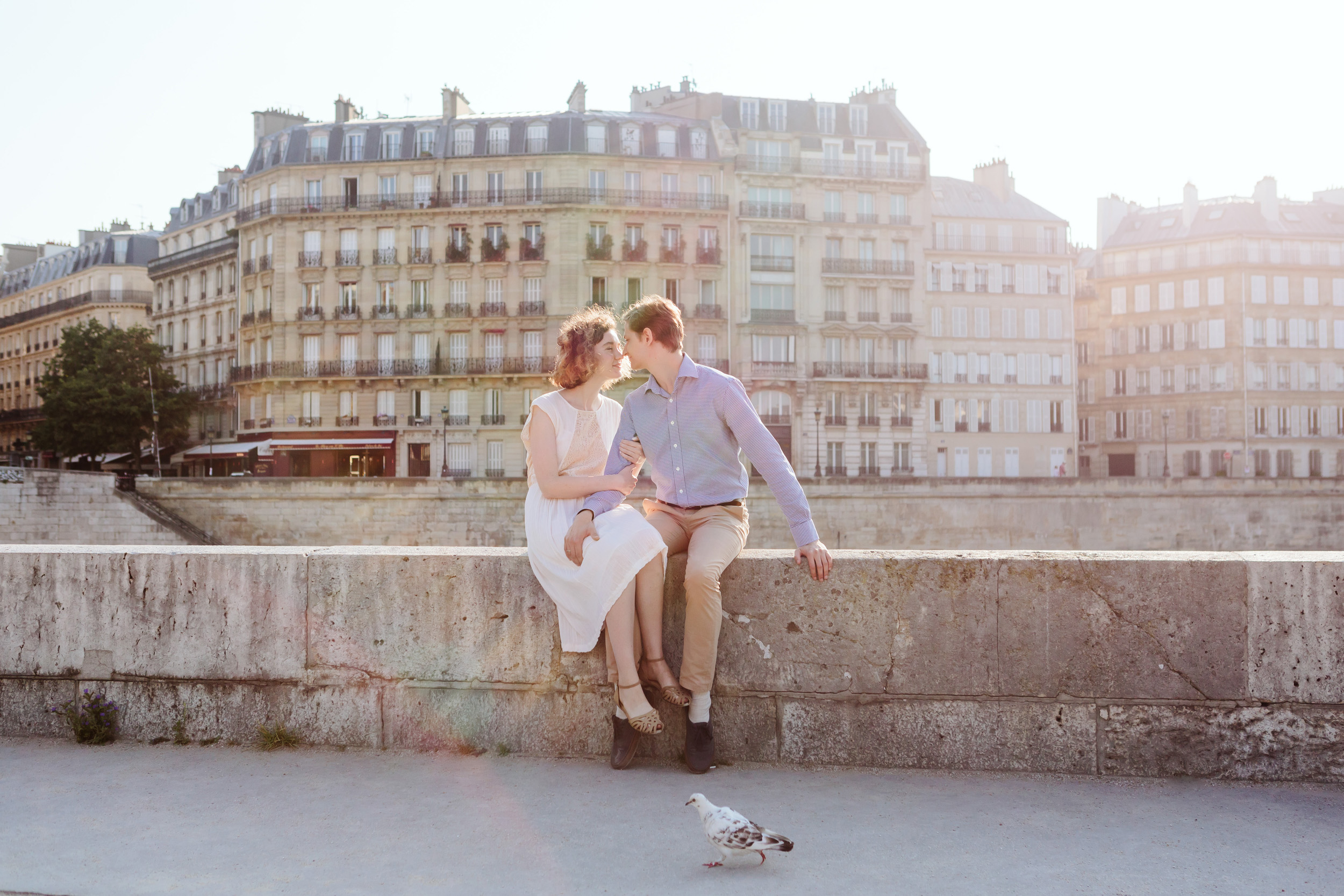 Couple in love kissing by Ile Saint Louis in Paris at sunrise with pigeon walking in the foreground captured by Paris Photographer Federico Guendel IheartParisFr
