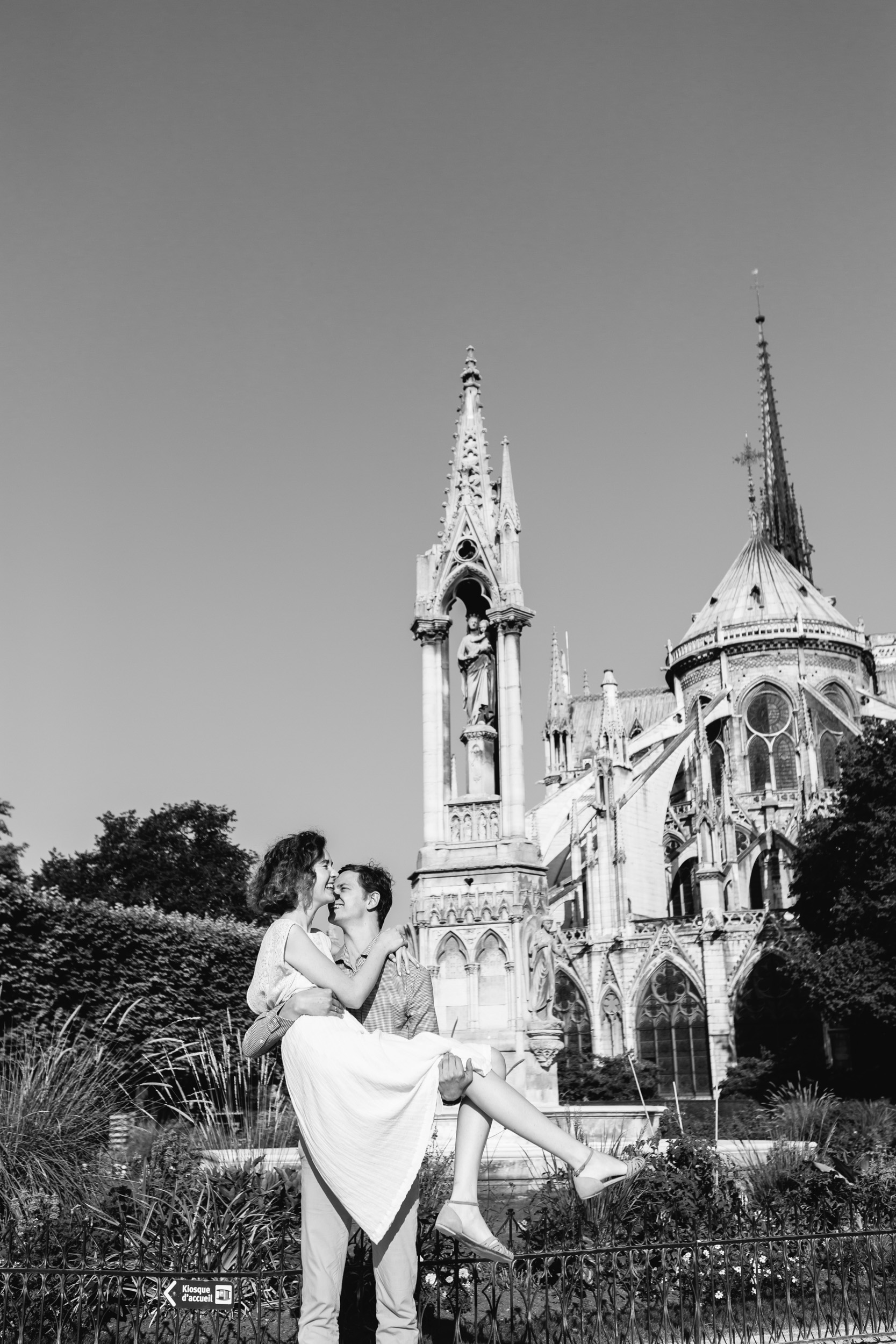 Man holding his wife in his arms by Notre Dame Cathedral garden in Paris - black and white photo captured by Paris Photographer Federico Guendel IheartParisFr