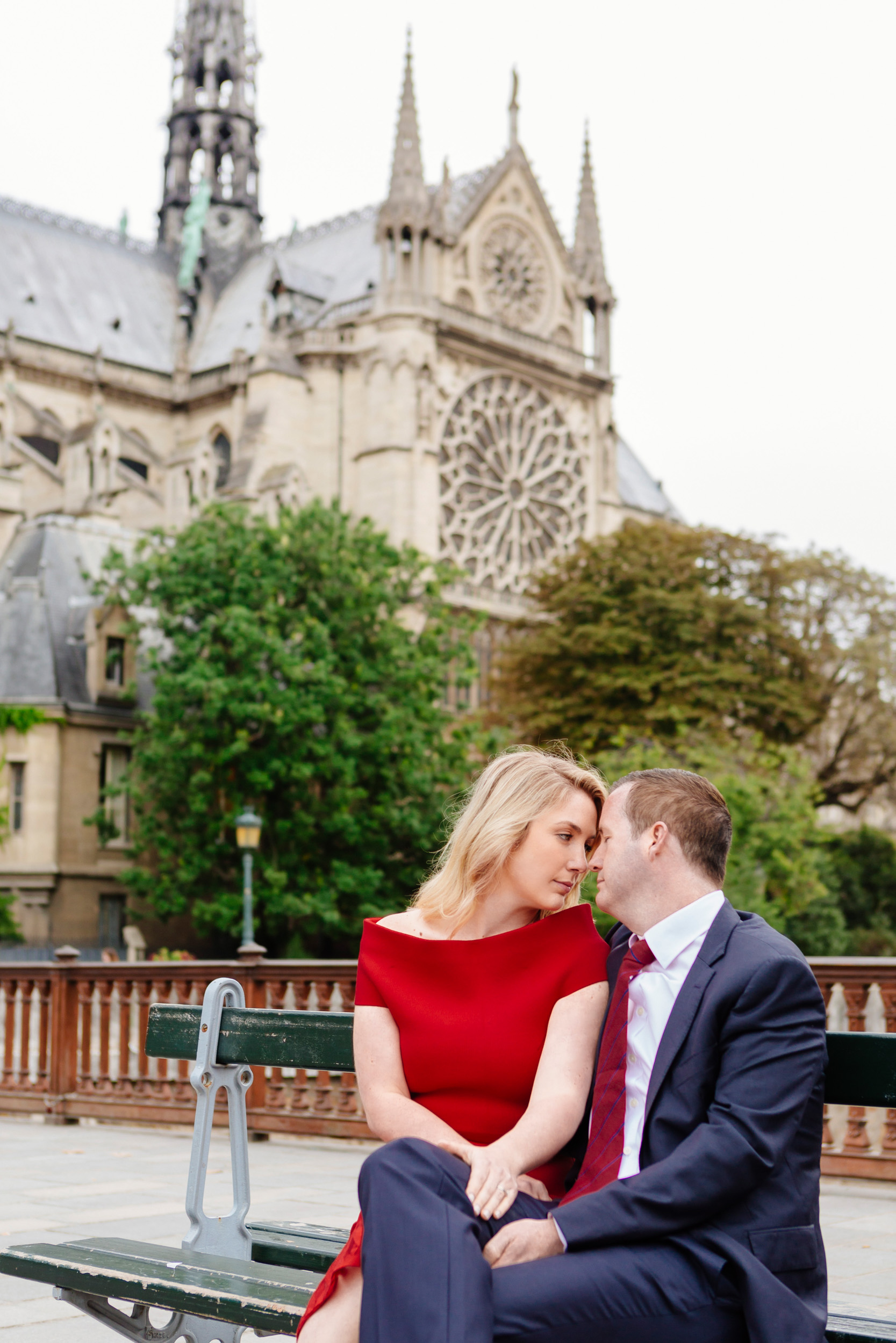Romantic portrait of a couple sitting on a bench with the view of Notre Dame Cathedral captured by Paris Photographer Federico Guendel www.iheartparis.fr