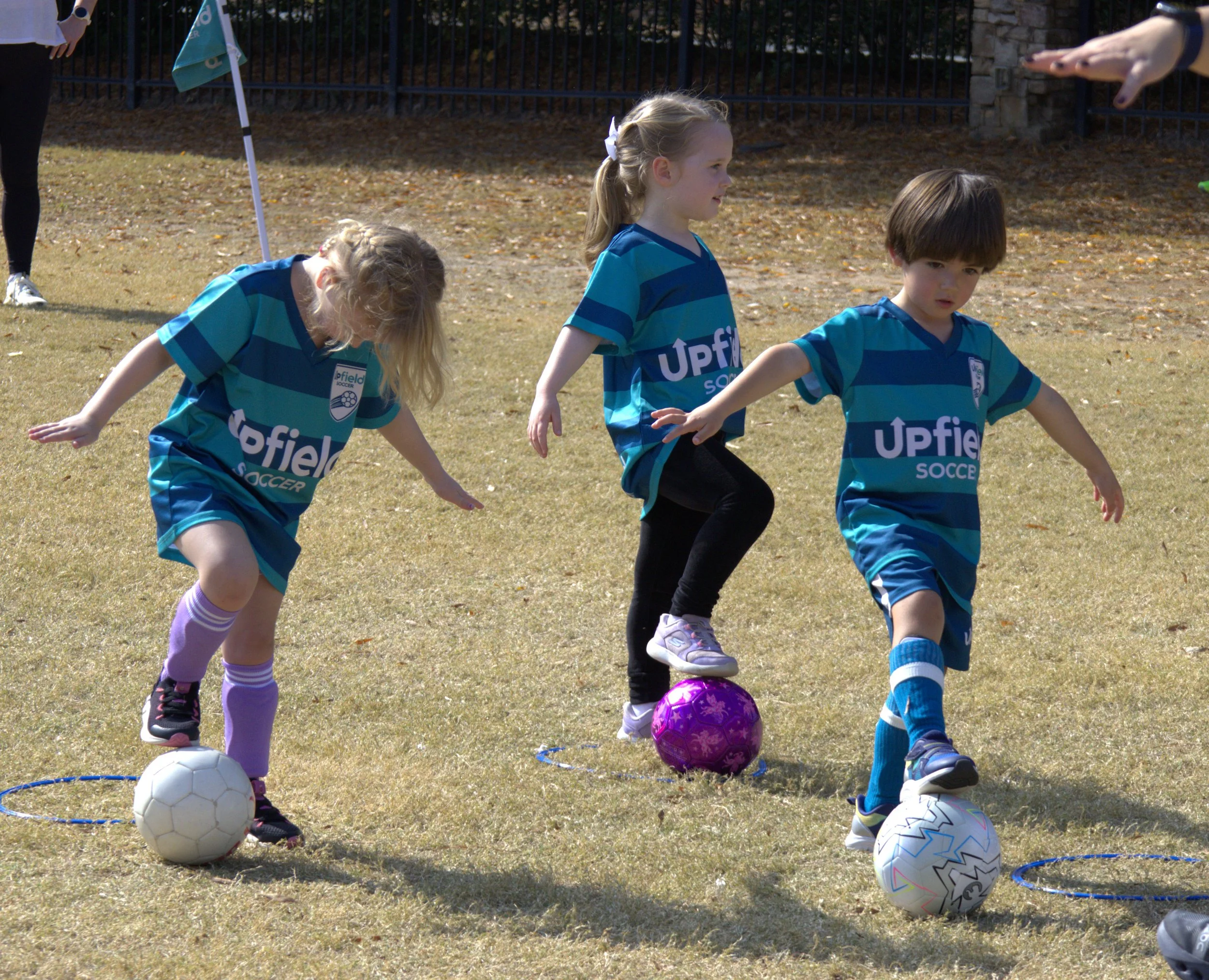 three kids with soccer balls balance with one foot on top