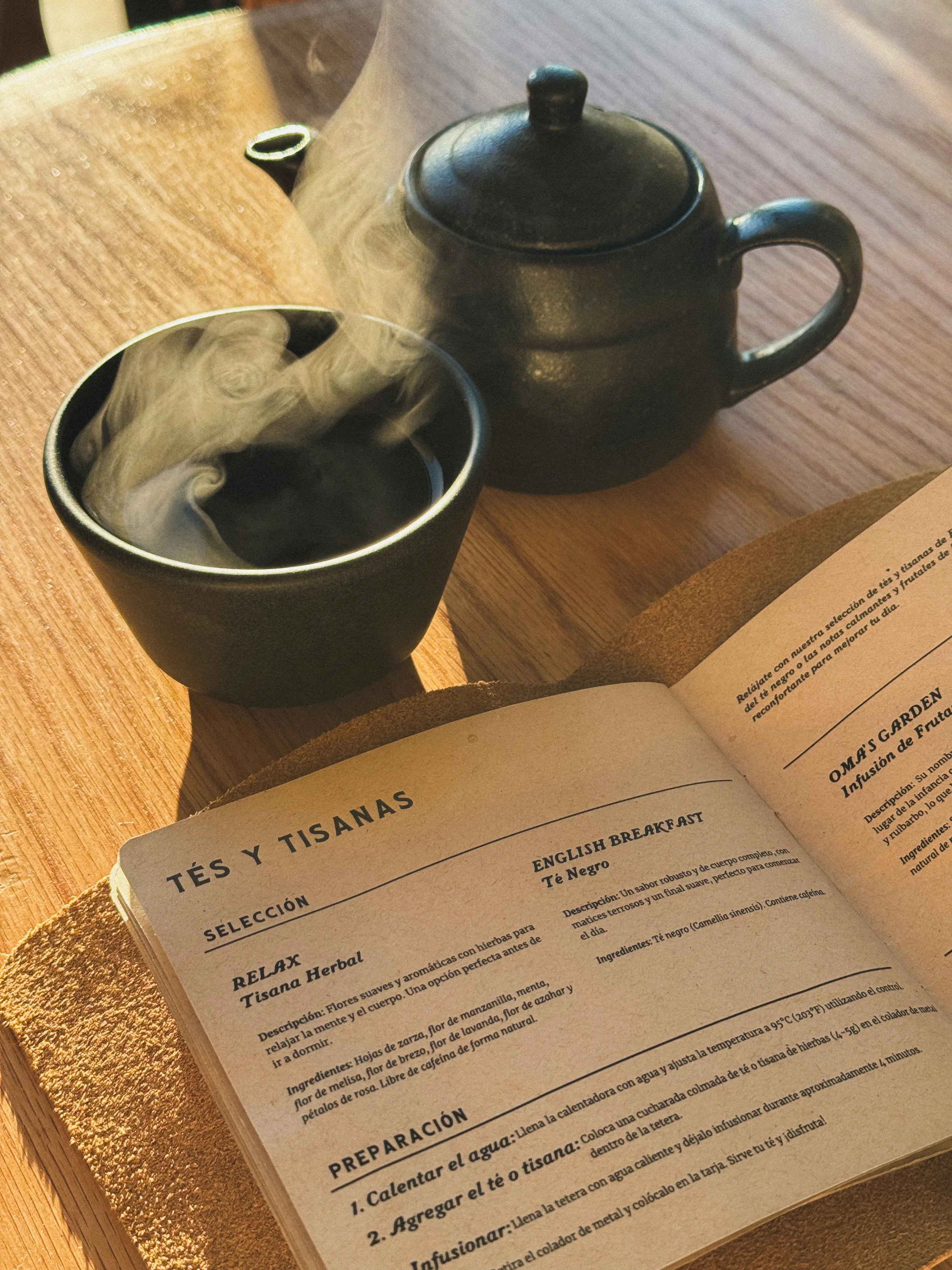 Black teapot with steaming cup of tea and té or tea menu bound in leather
