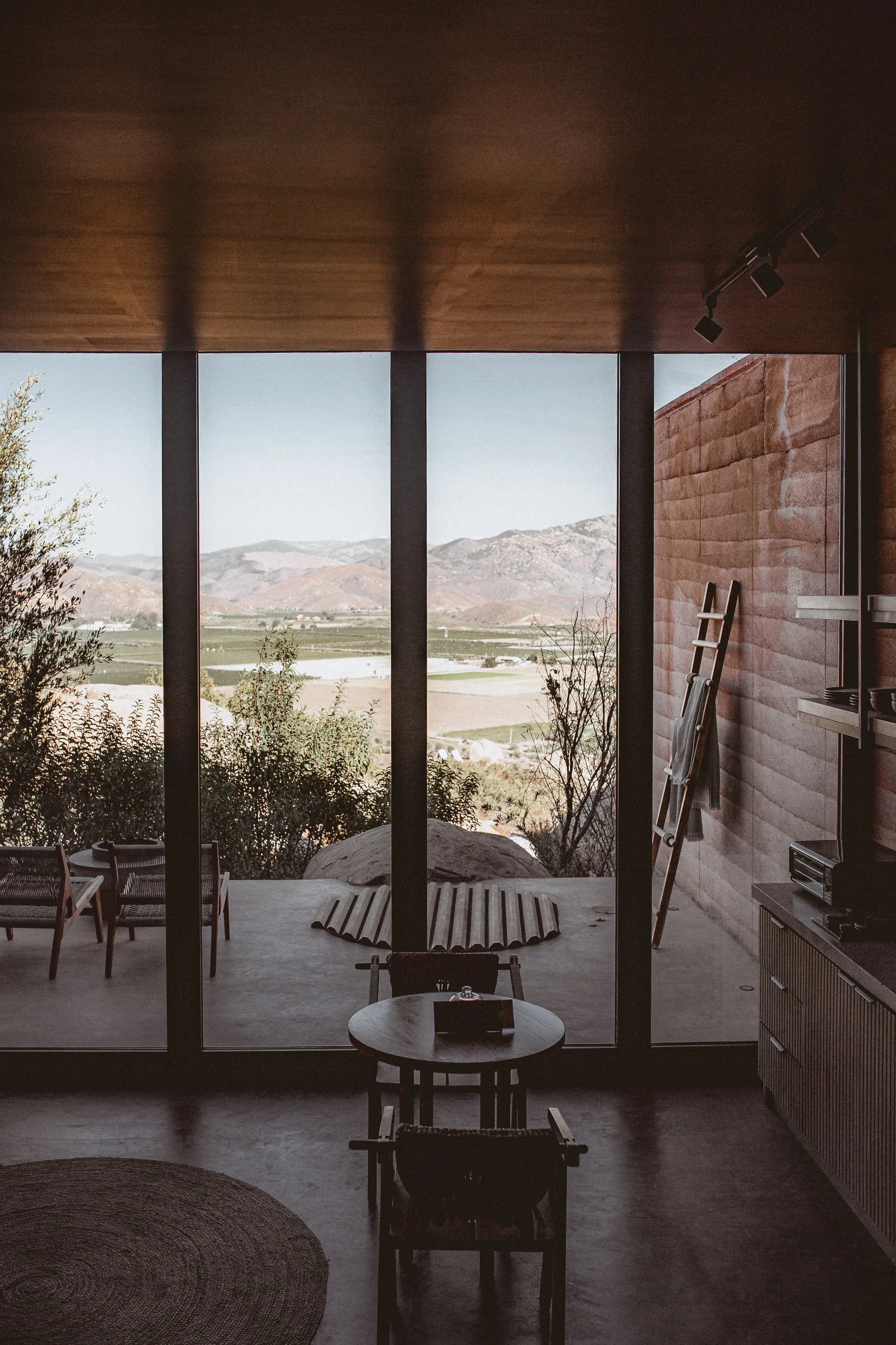 Studio with window wall, small table. Outside two chairs, fire pit, cover over jacuzzi, towel ladder and view of valley at Mira Earth Studios