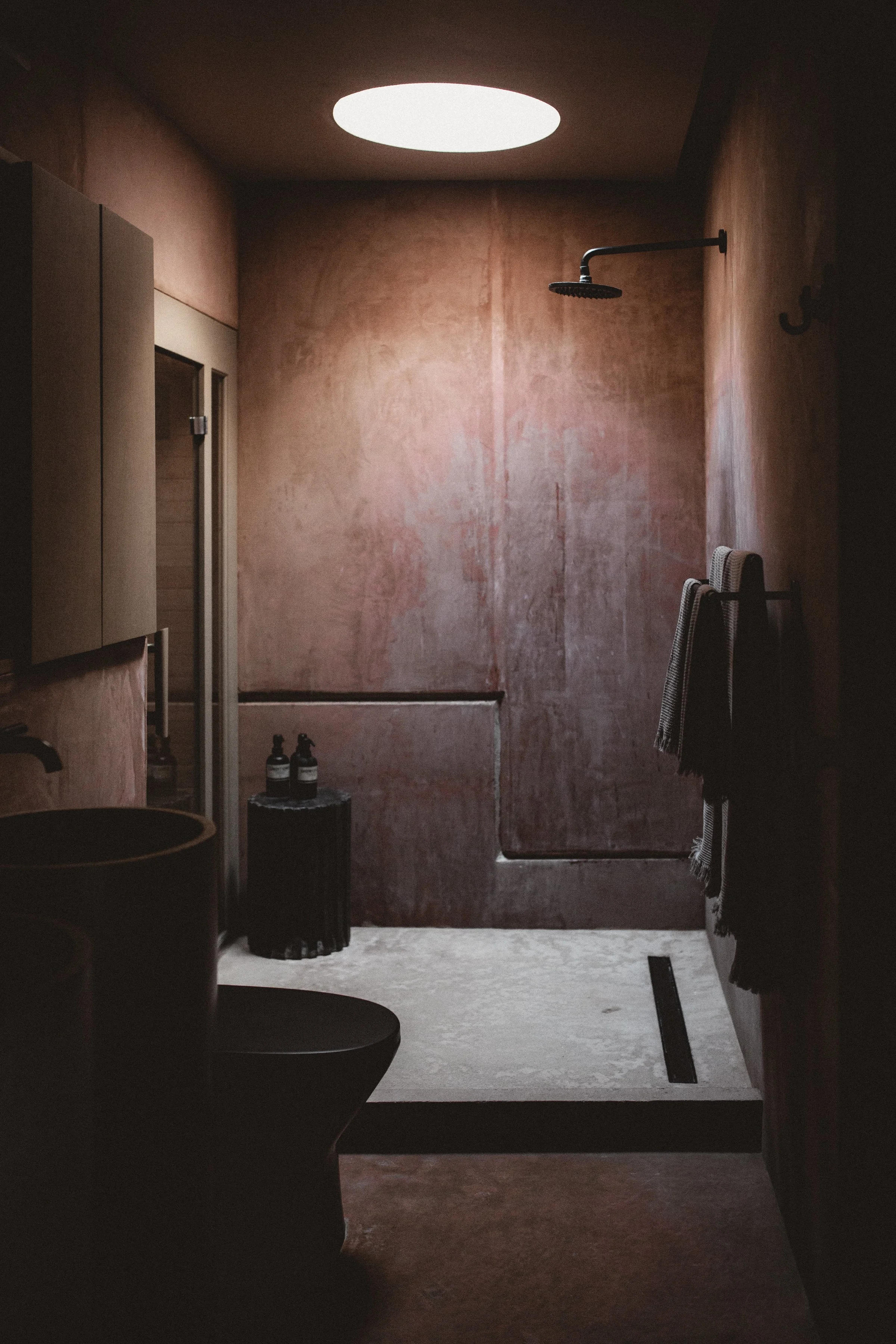 Open shower with round skylight and rose colored earthen walls