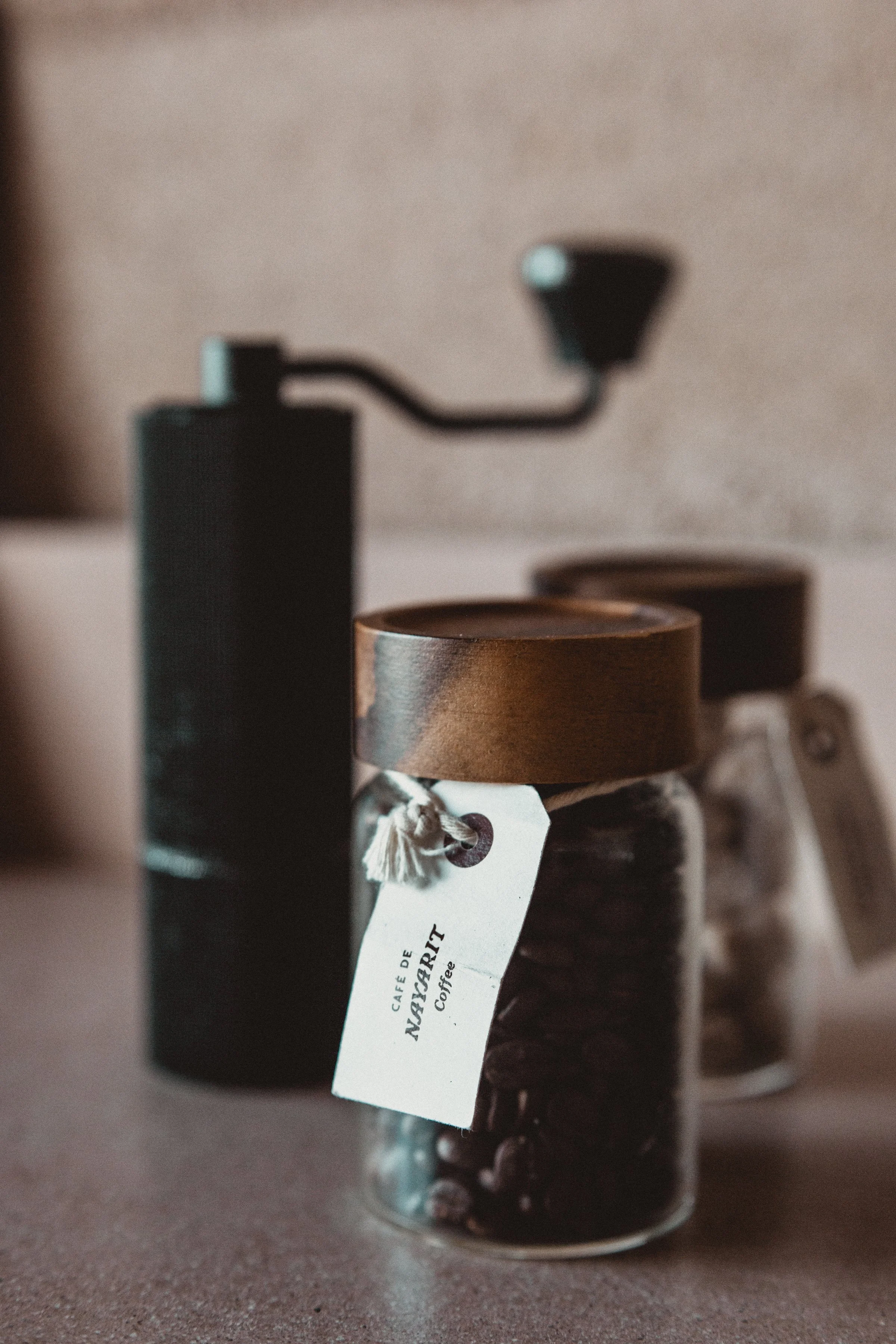 Two small jars of coffee beans with label and grinder in background