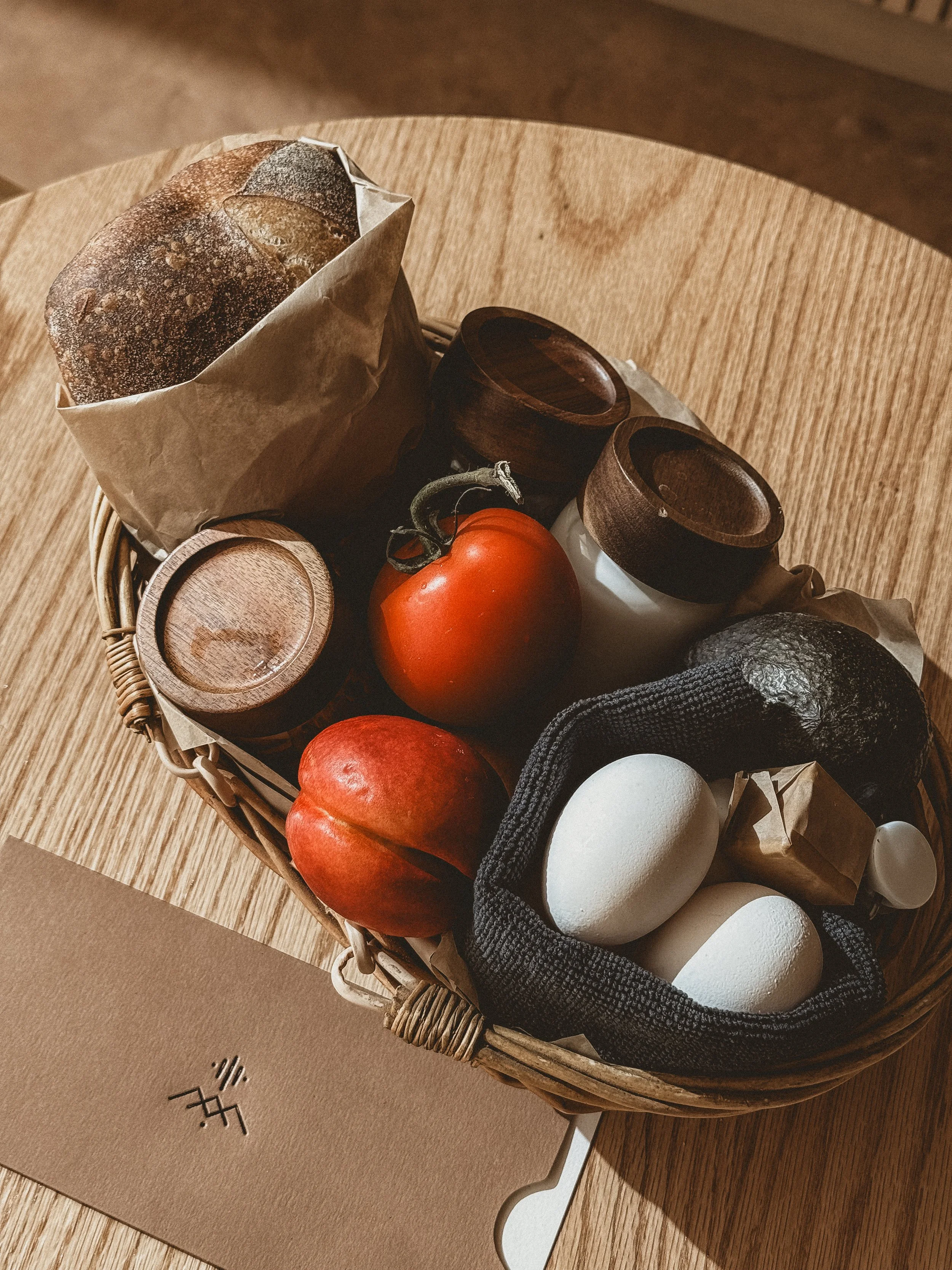 Basket of chilaquiles ingredients: tomatoes, eggs, avocado, with jars of crema, salsa and chips including loaf of bread