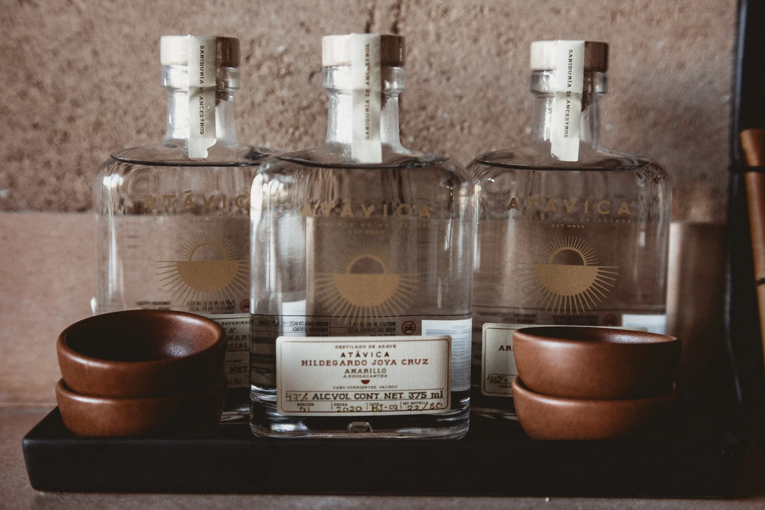 Three bottle of Atávica tequila on a black tray with small wood bowls