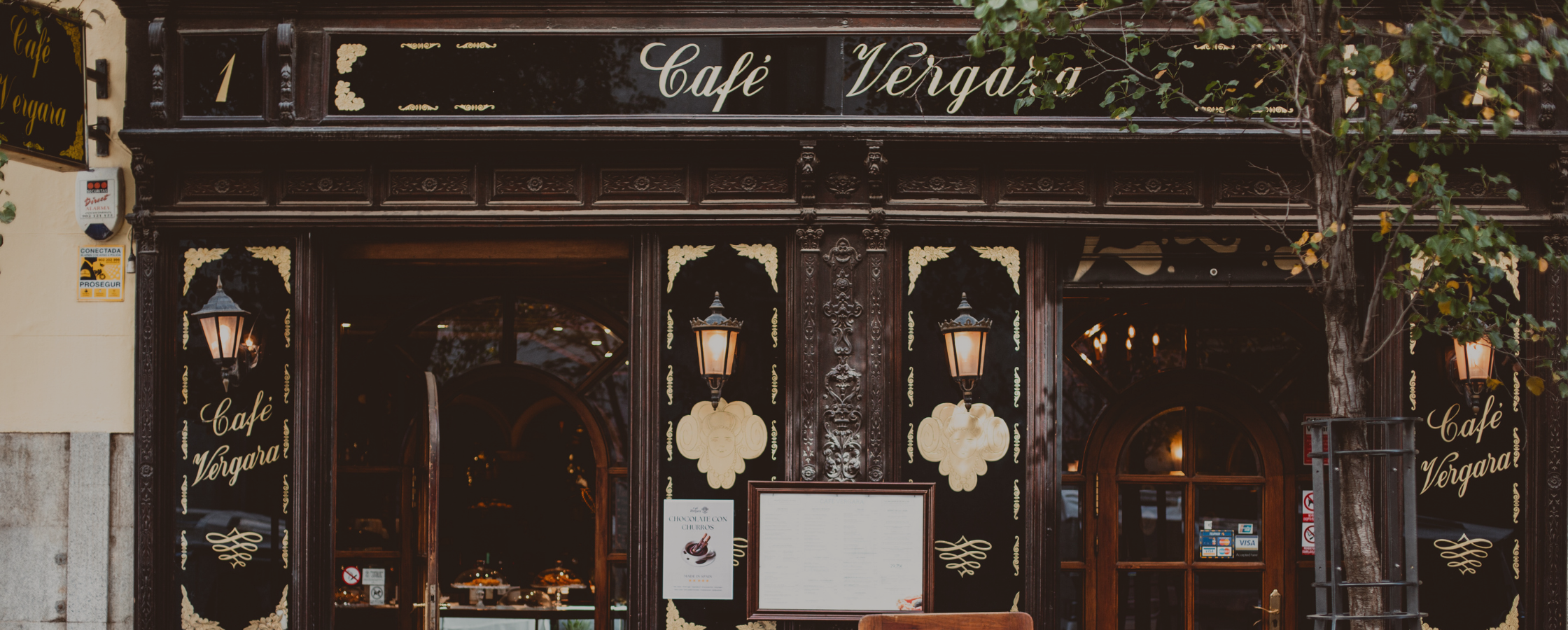Facade of Café Vergara with wood details, arched doorways and lit wall sconces