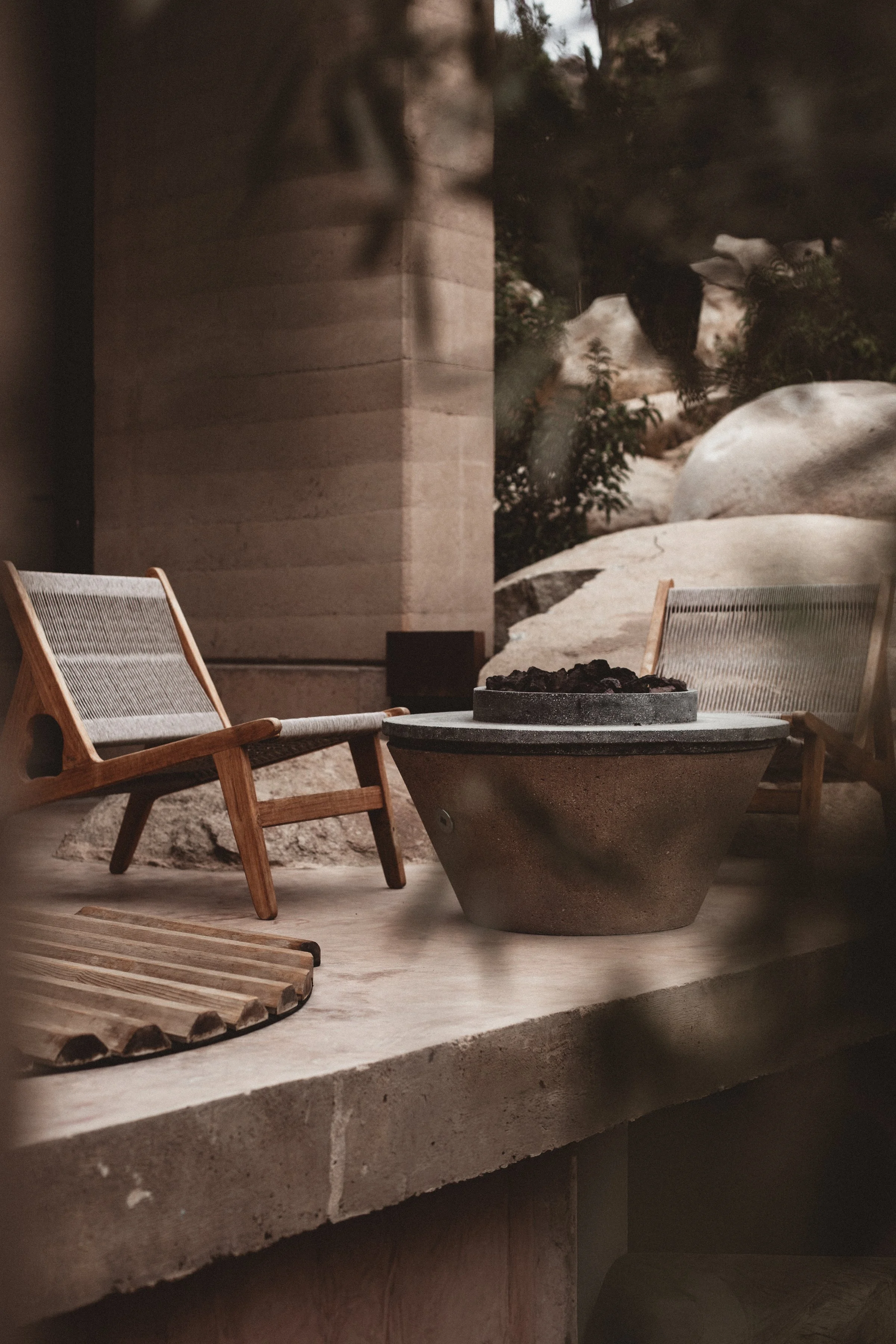 Peek at balcony though tree leaves of woven chairs, stone fire pit and wood jacuzzi cover at Mira Earth Studios