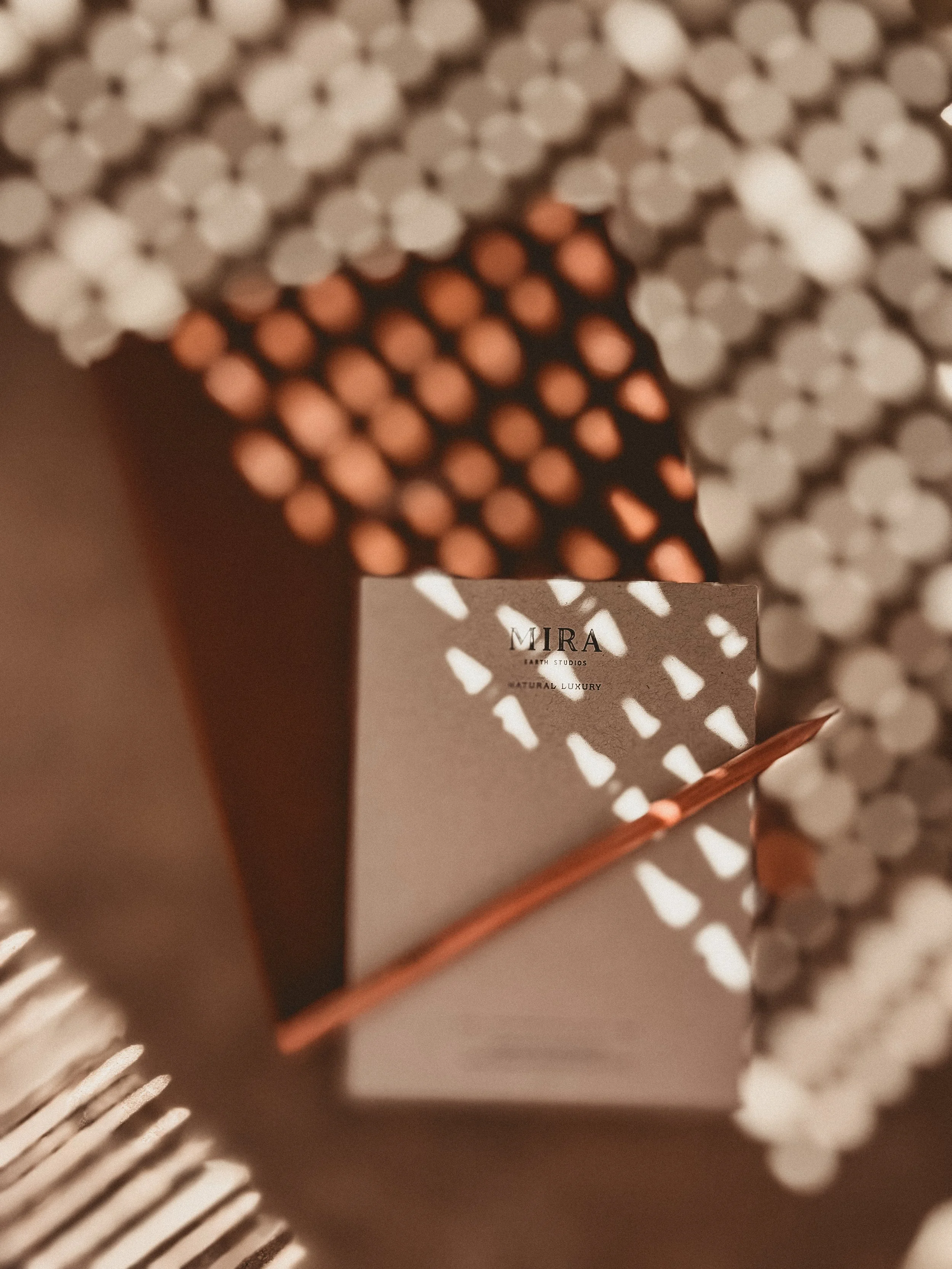 Speckled shadows over leather journal, Mira notepad and pencil