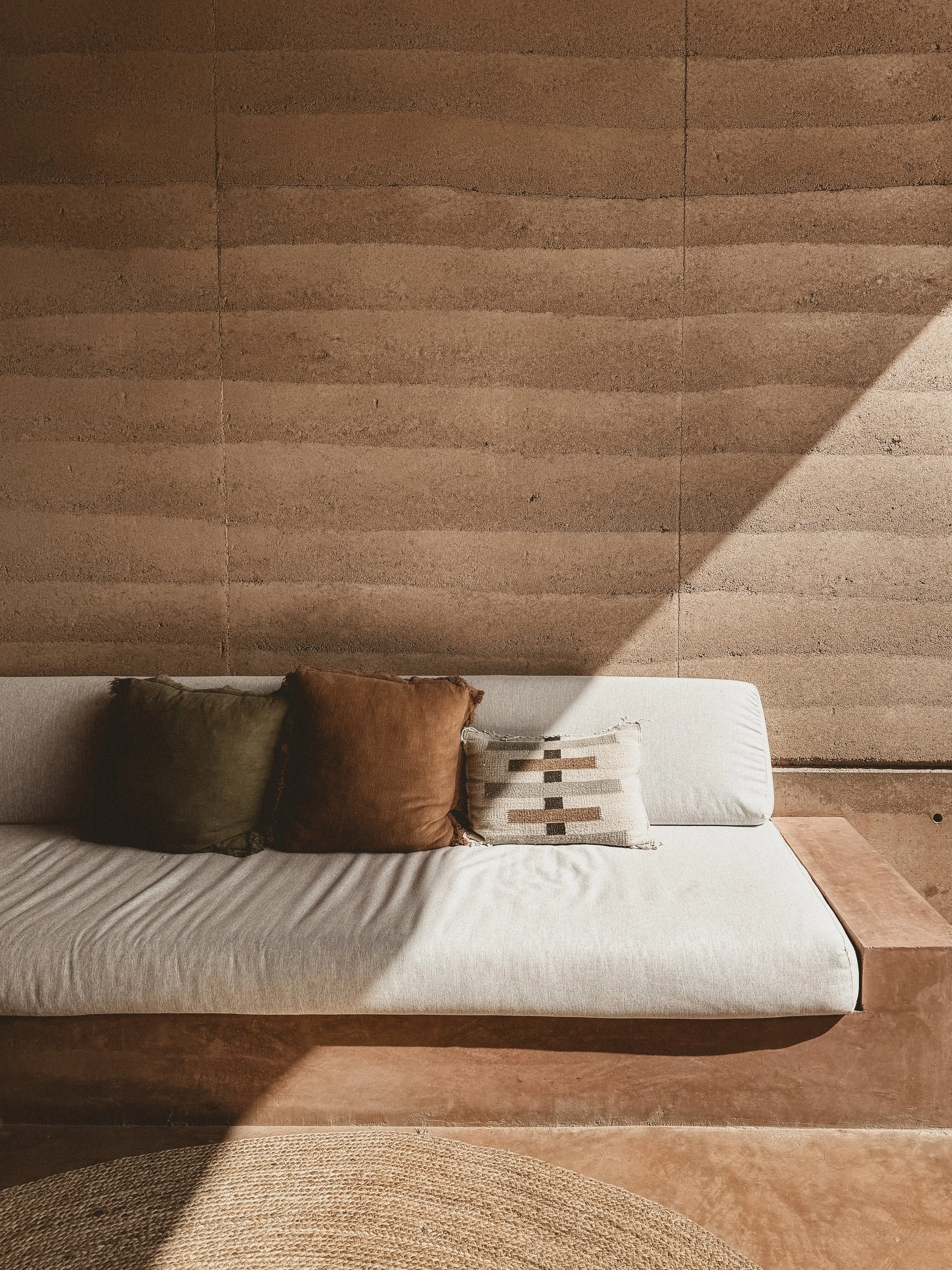 White cushion earthen couch with dark olive green, sienna brown and stripped patterned pillows