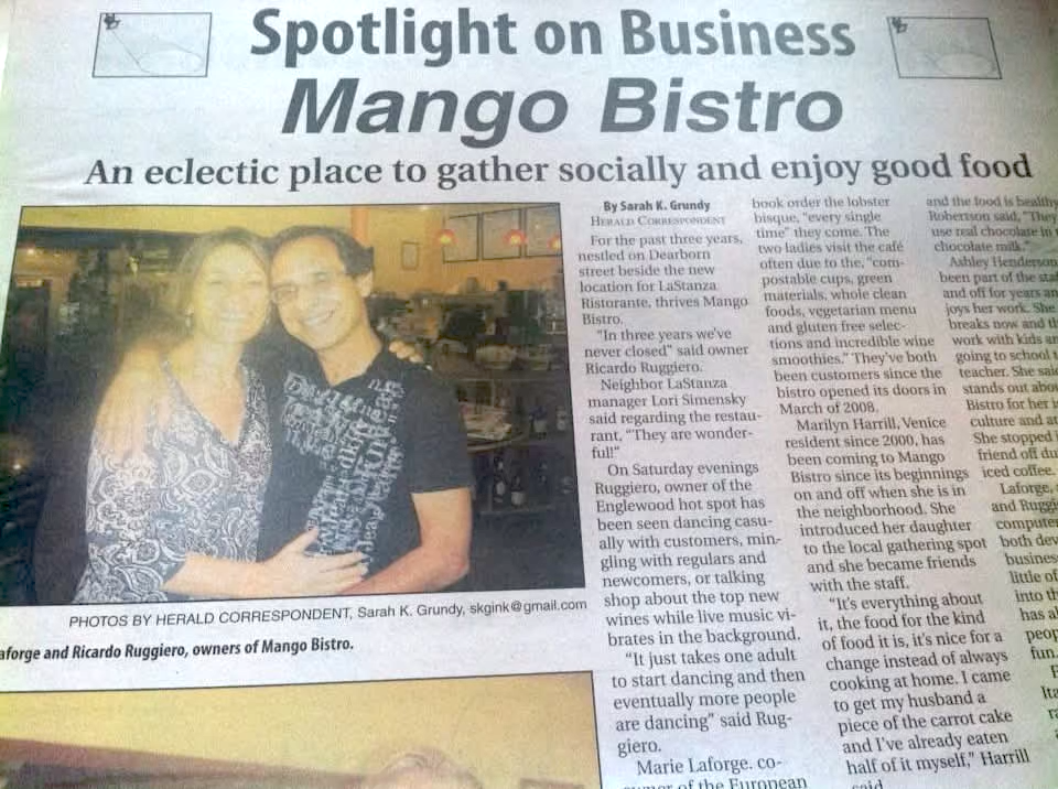 Newspaper article titled "Spotlight on Business Mango Bistro" featuring a photo of two women, one wearing a patterned blouse and the other in a black T-shirt, standing inside a restaurant.