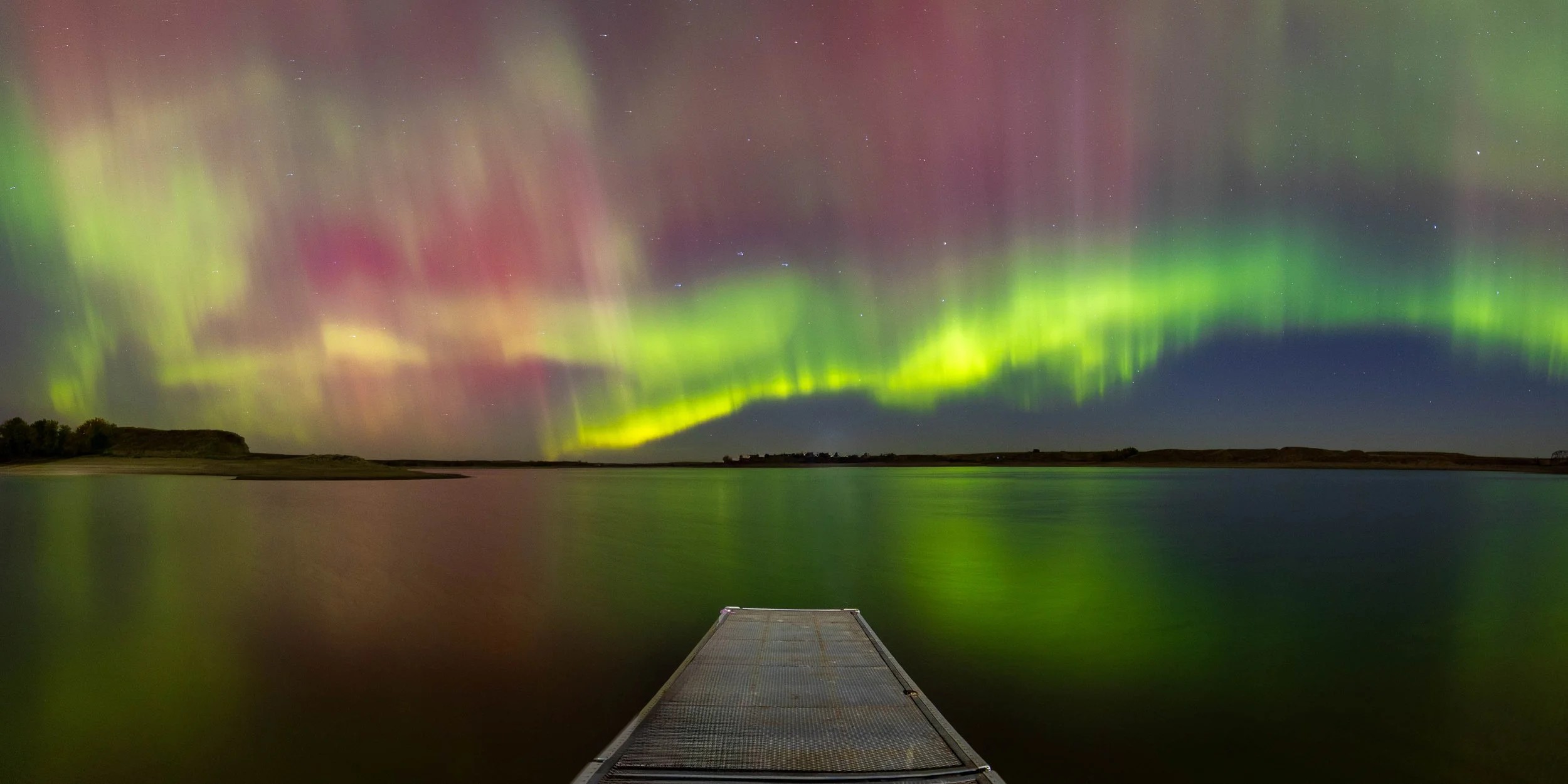Northern lights over a lake with a small dock in the foreground